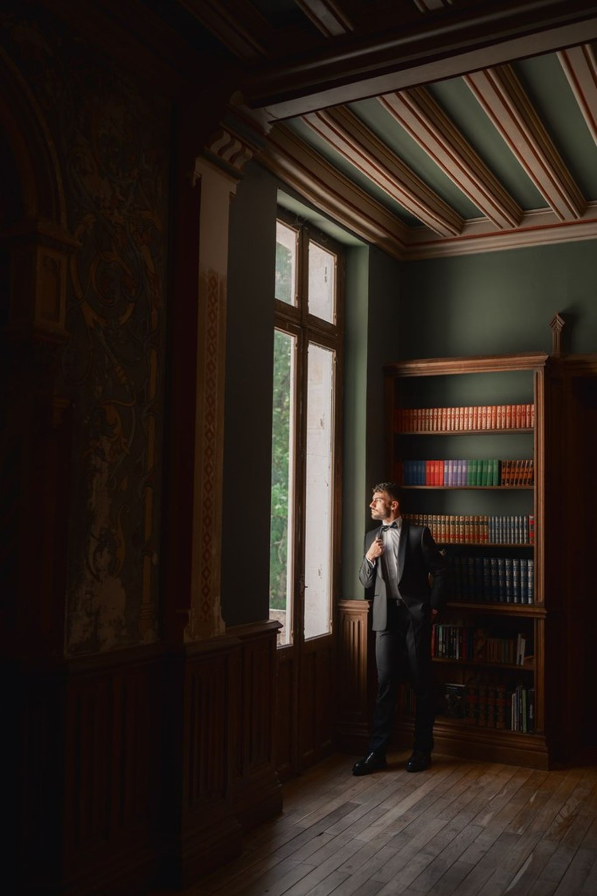 Blush and fuchsia styled shoot at Château du Causse, Occitanie, the groom in a black tuxedo in a panelled library