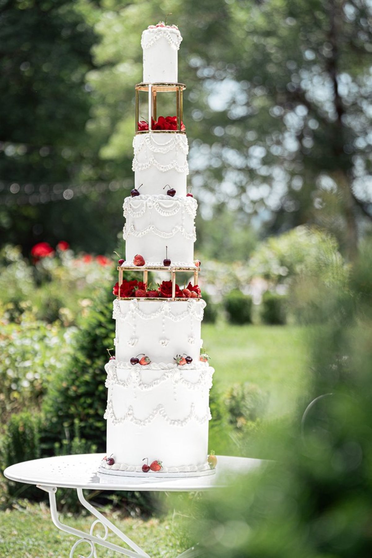 Blush and fuchsia styled shoot at Château du Causse, Occitanie, a tall tiered white cake with strawberries in the rose garden