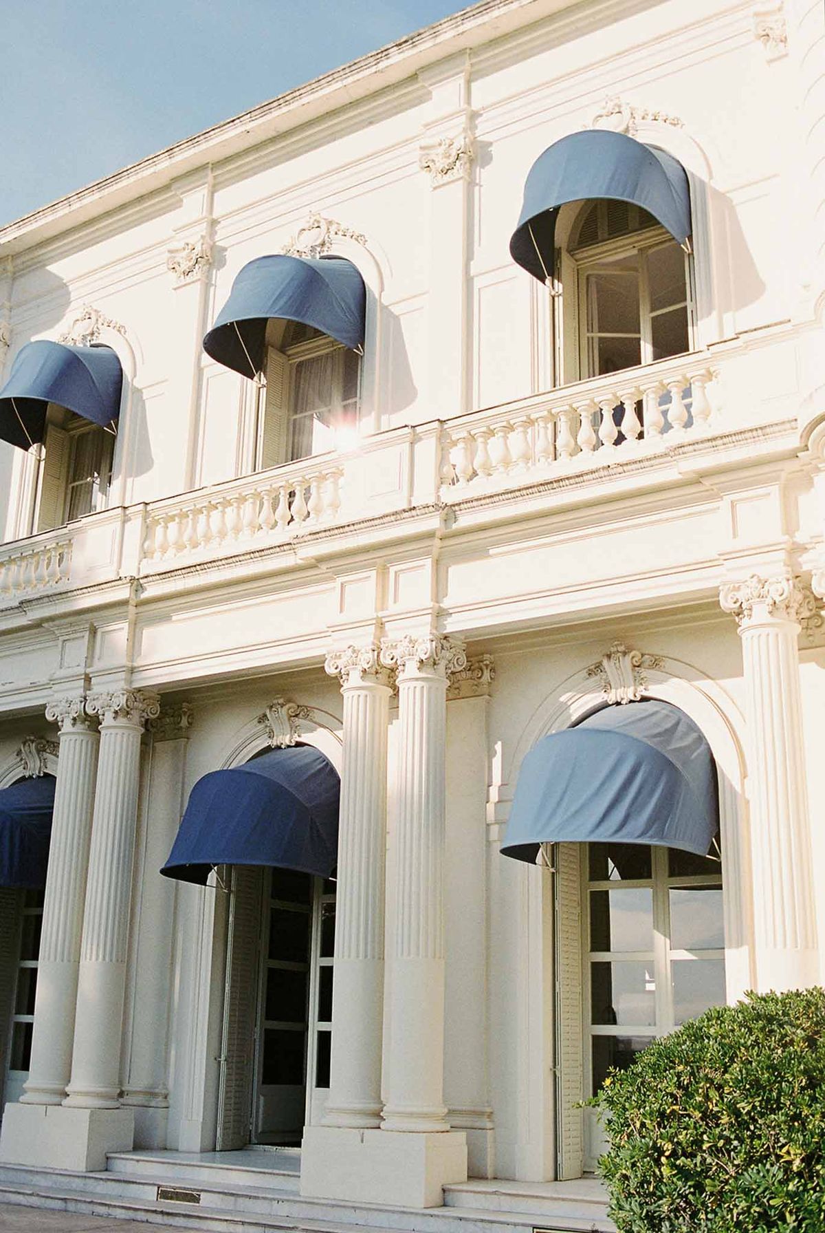 Villa facade with blue awnings and stone columns at Domaine Rocabella, French Riviera