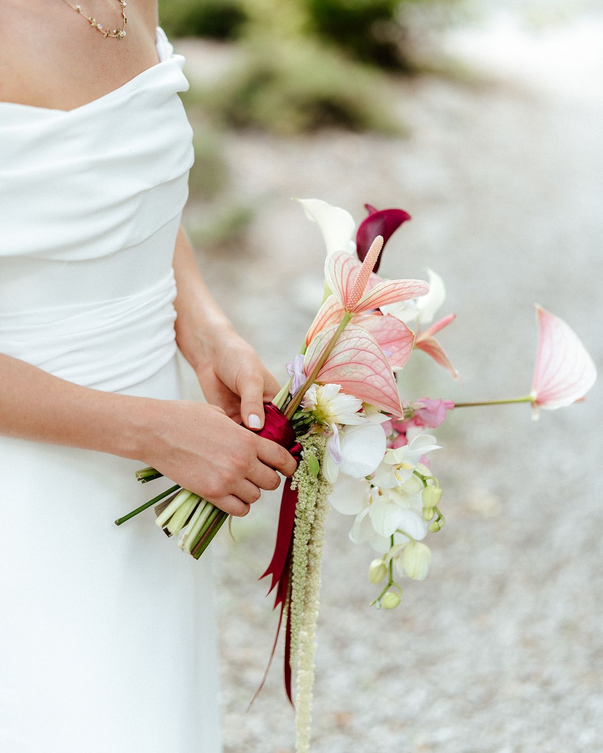 The bride's hands holding a bouquet of anthurium, orchid and burgundy calla