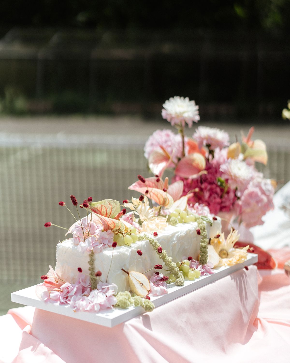 White cake dressed with flowers on a pink draped table on the tennis court