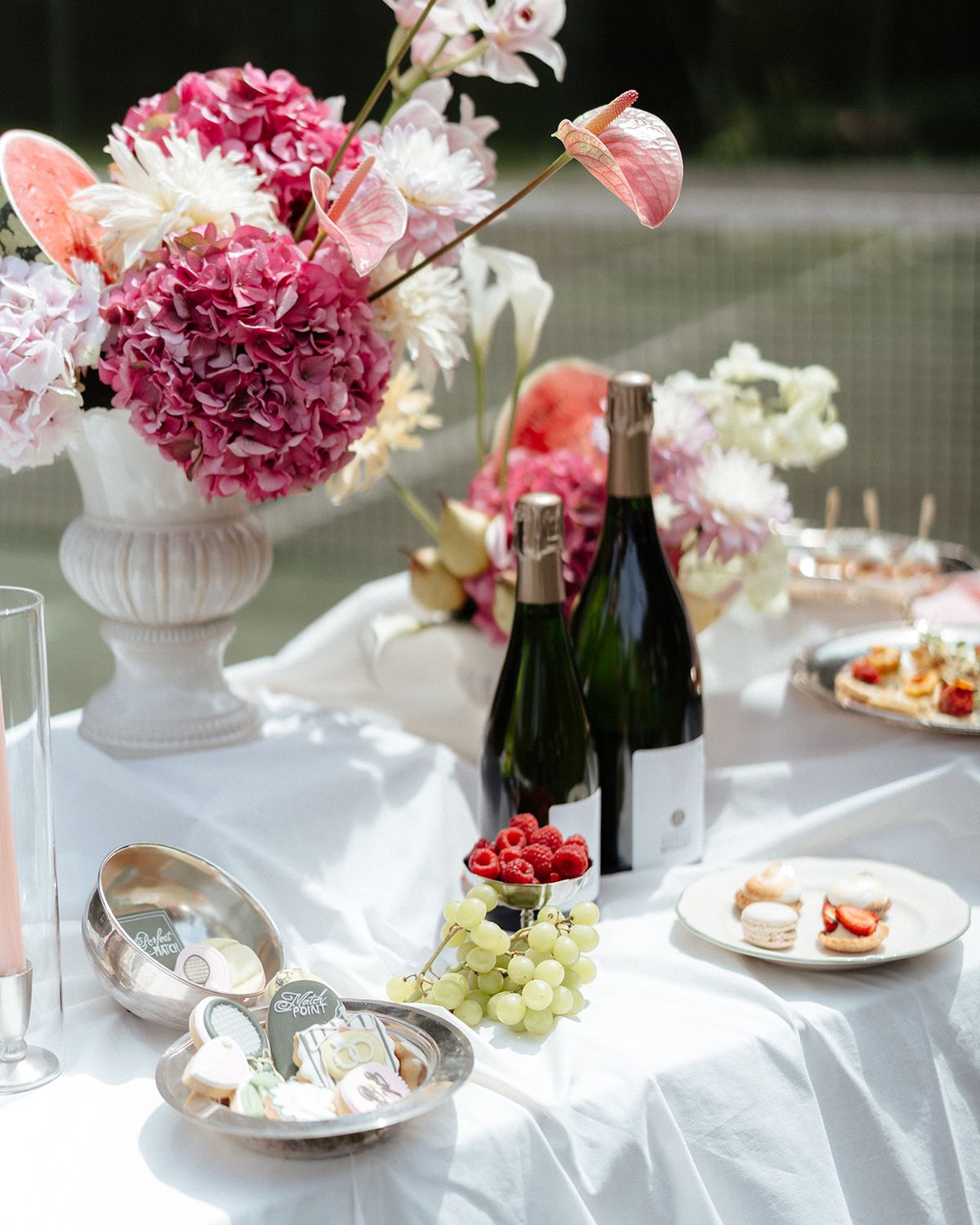 White urn of pink hydrangea and anthurium beside champagne bottles and silver dishes