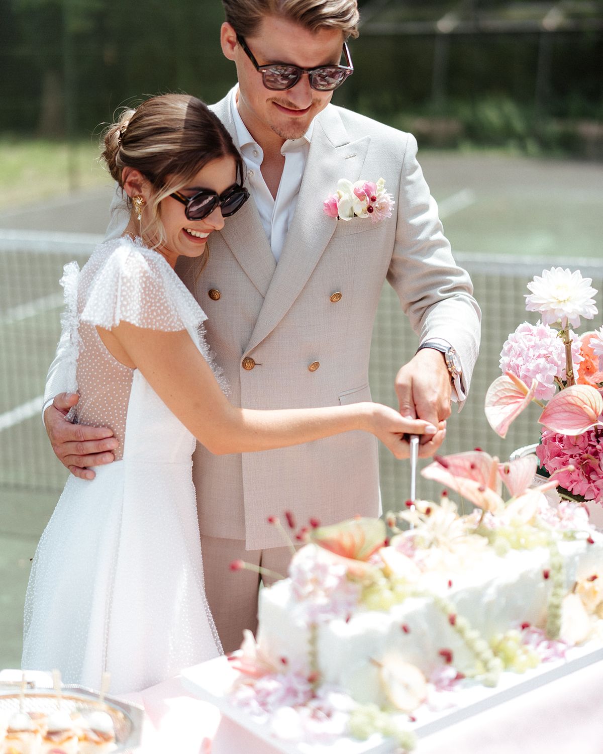 Couple in sunglasses cutting a flower dressed cake on the tennis court