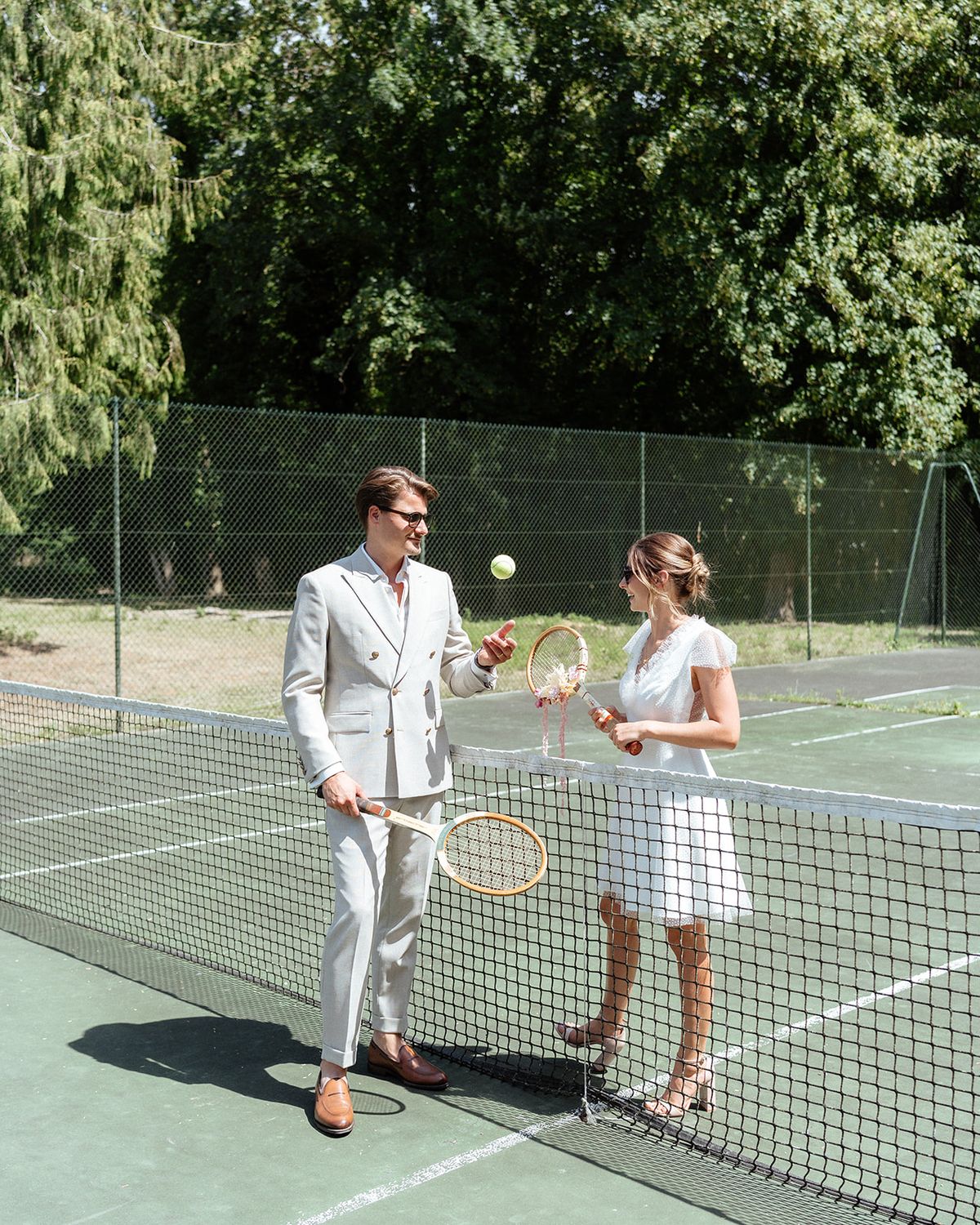 Bride and groom facing each other across the tennis net with wooden rackets