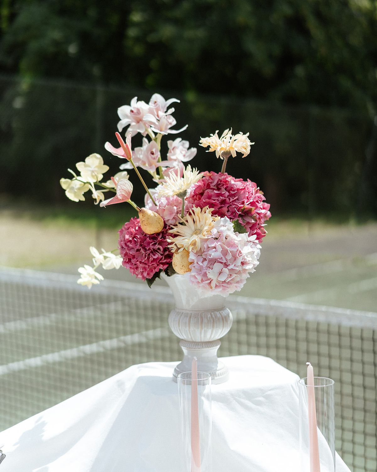 White urn of pink hydrangea, orchid and anthurium on a draped table at the tennis net