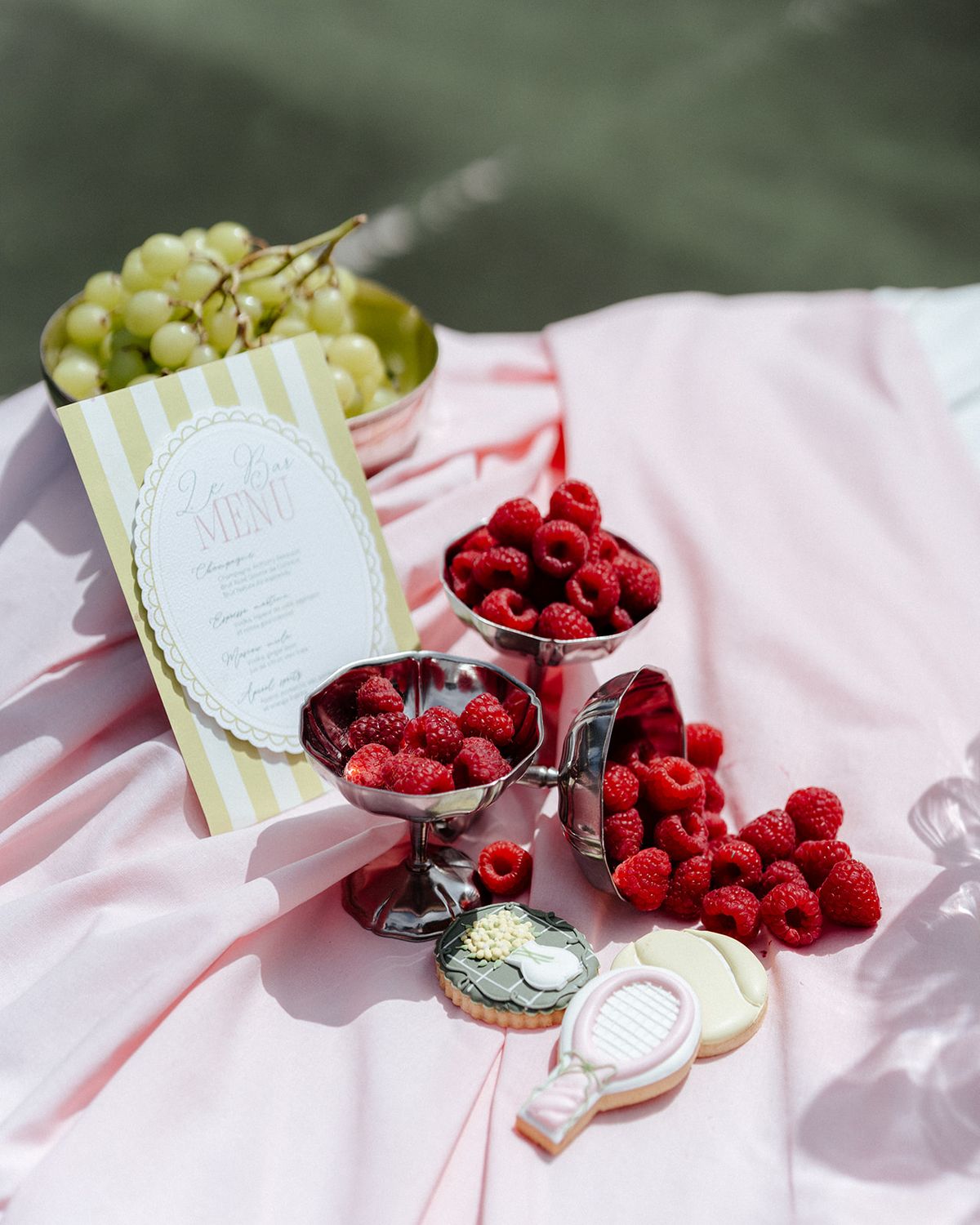 Raspberries in silver cups with iced biscuits and a menu card on a pink cloth
