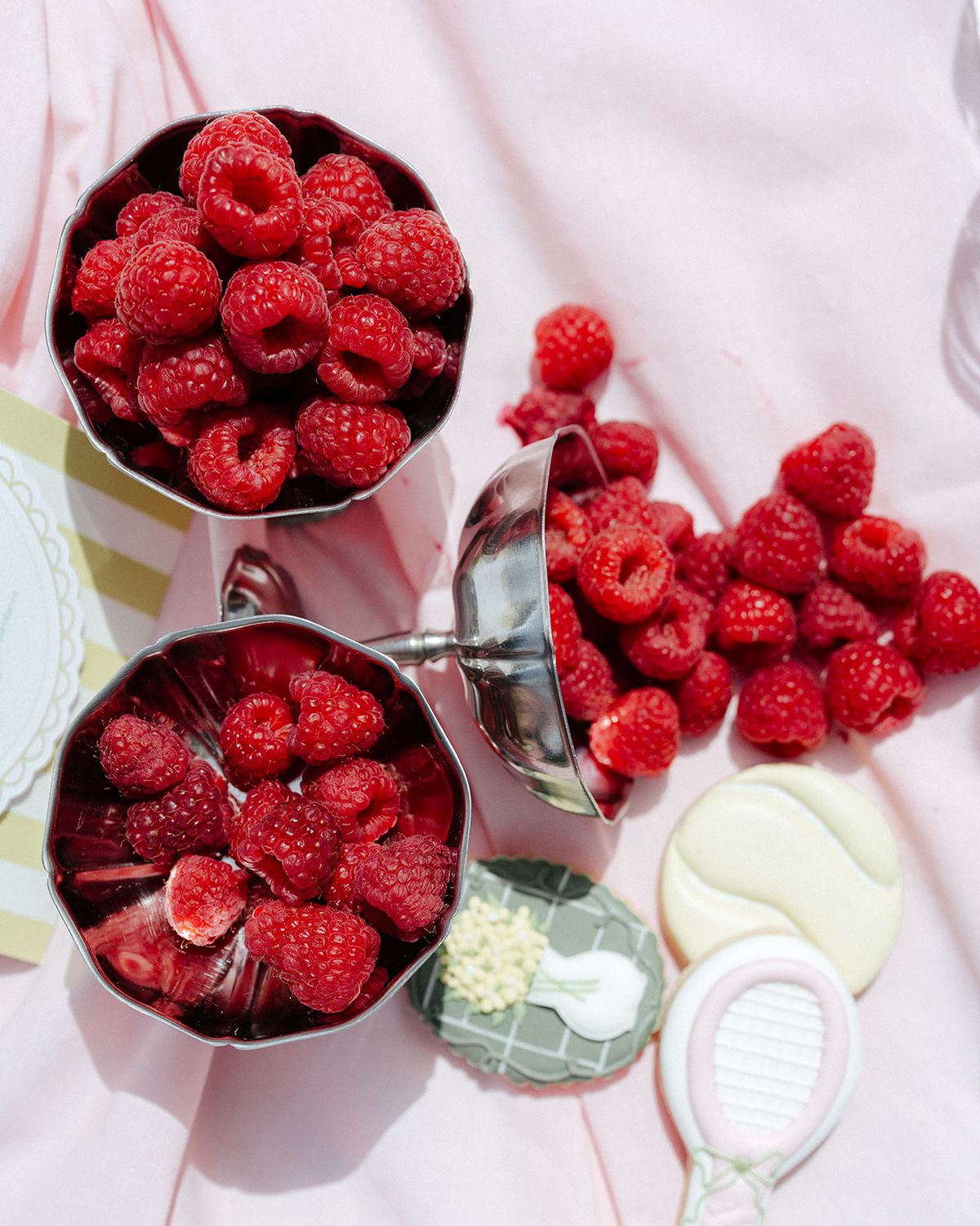 Silver cups of raspberries beside iced biscuits shaped as tennis rackets