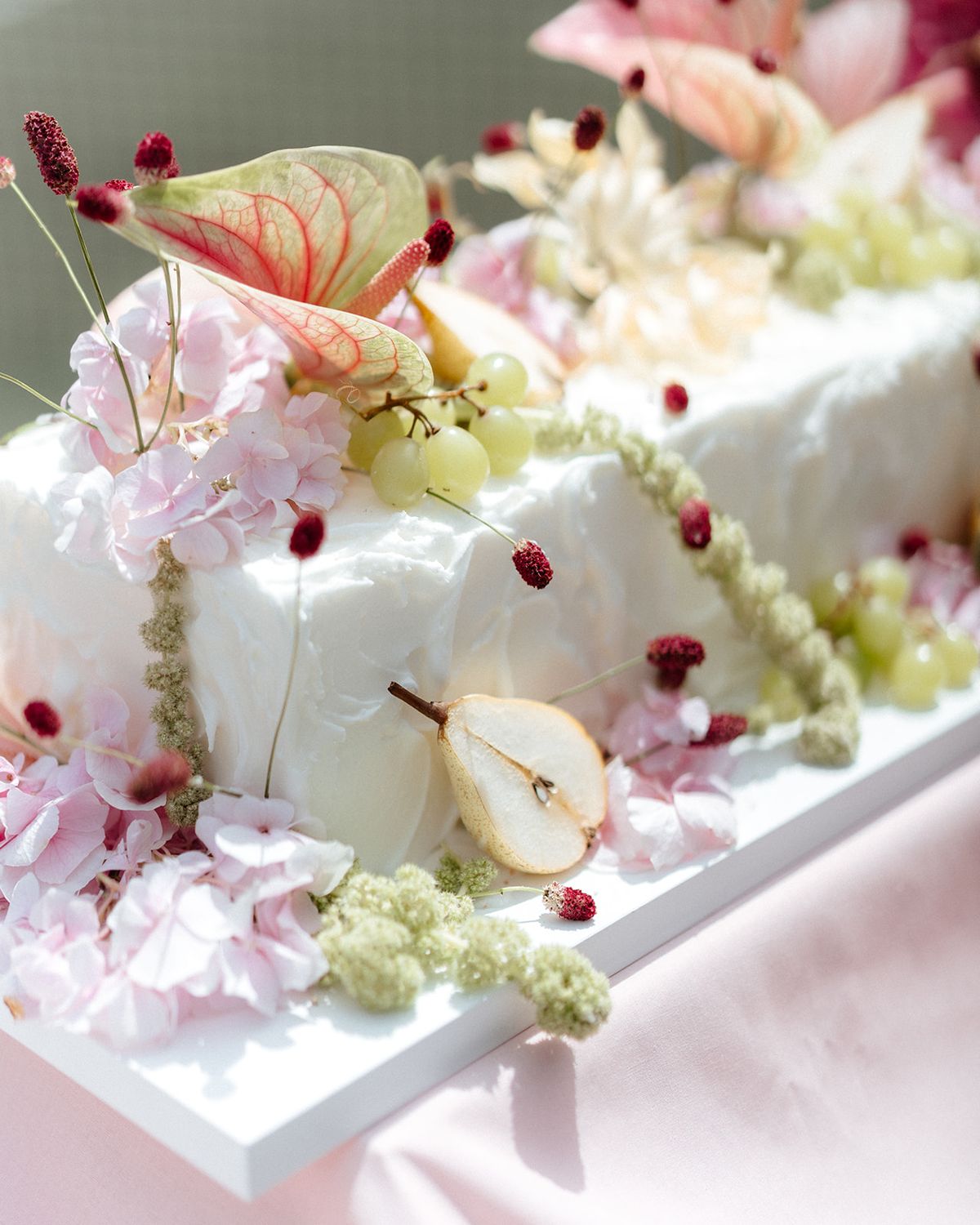 Close view of a white cake dressed with anthurium, grapes and sliced pear