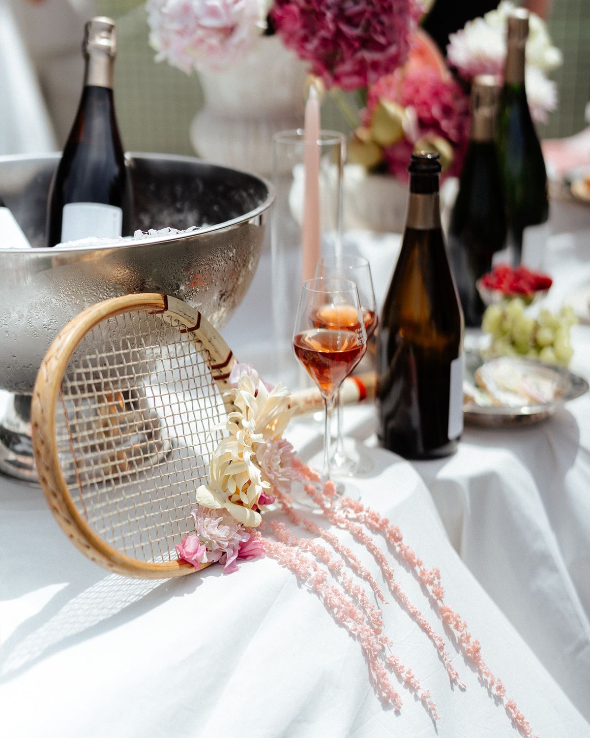 A tennis racket trimmed with flowers resting beside champagne bottles in a silver bucket
