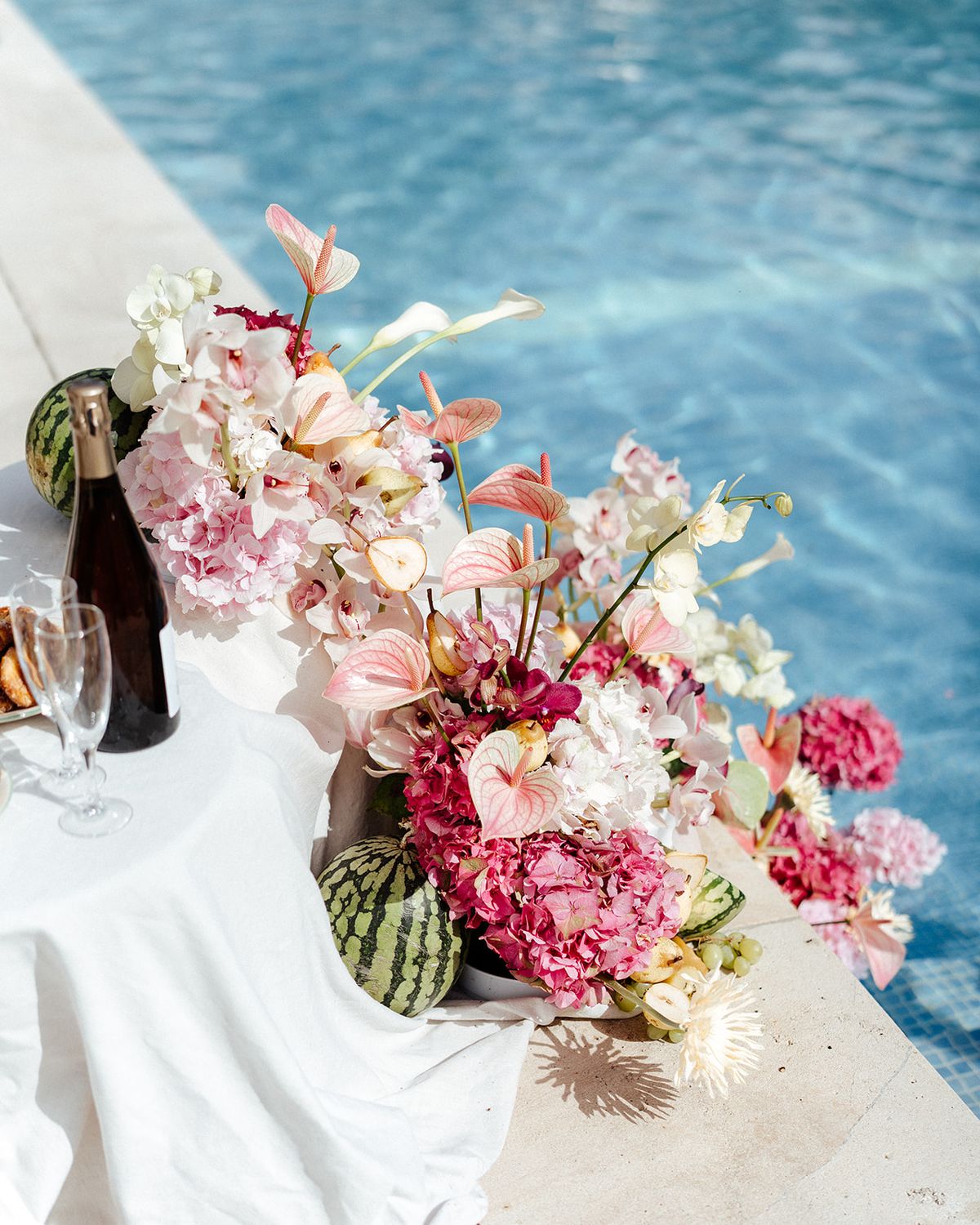 Poolside arrangement of anthurium, hydrangea and small watermelons beside champagne coupes