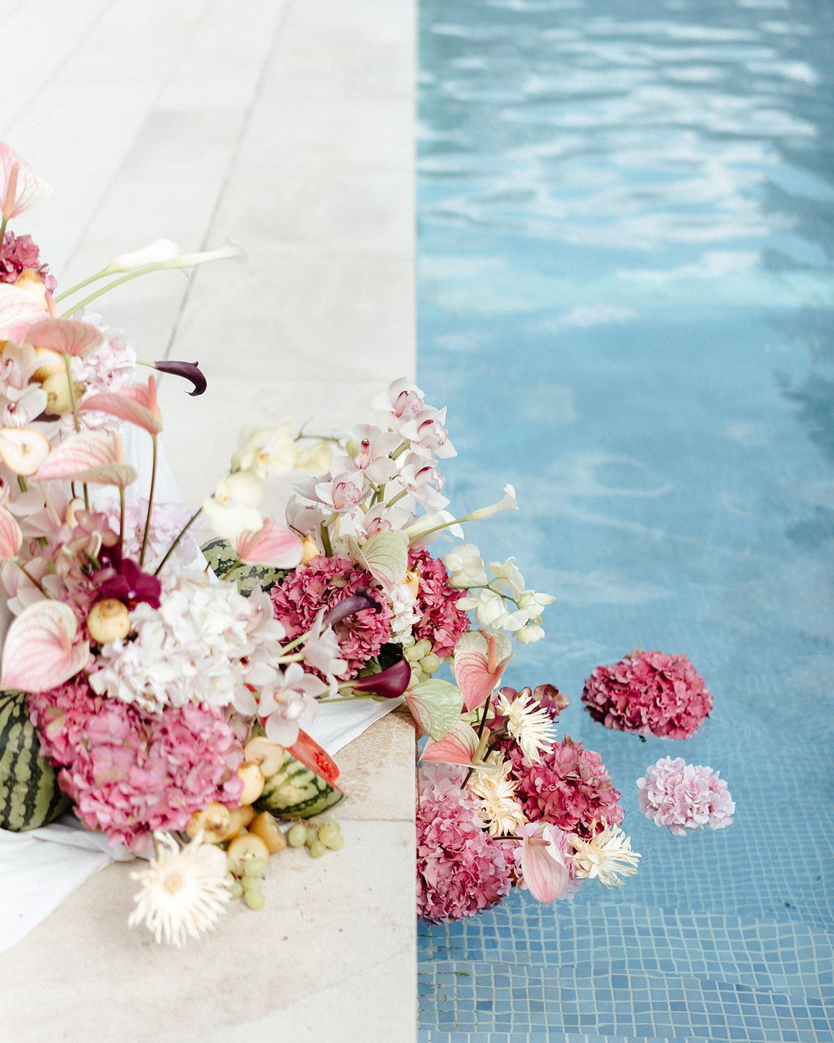 Pink hydrangea heads floating on a swimming pool beside a poolside floral arrangement