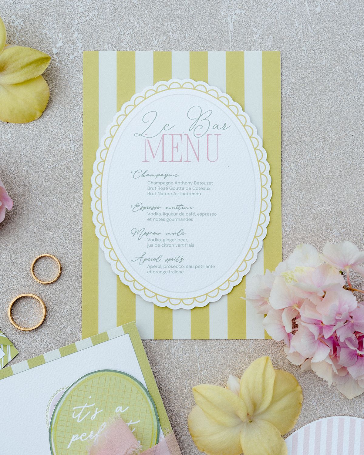 Yellow and white striped menu card with a scalloped edge beside gold rings and hydrangea