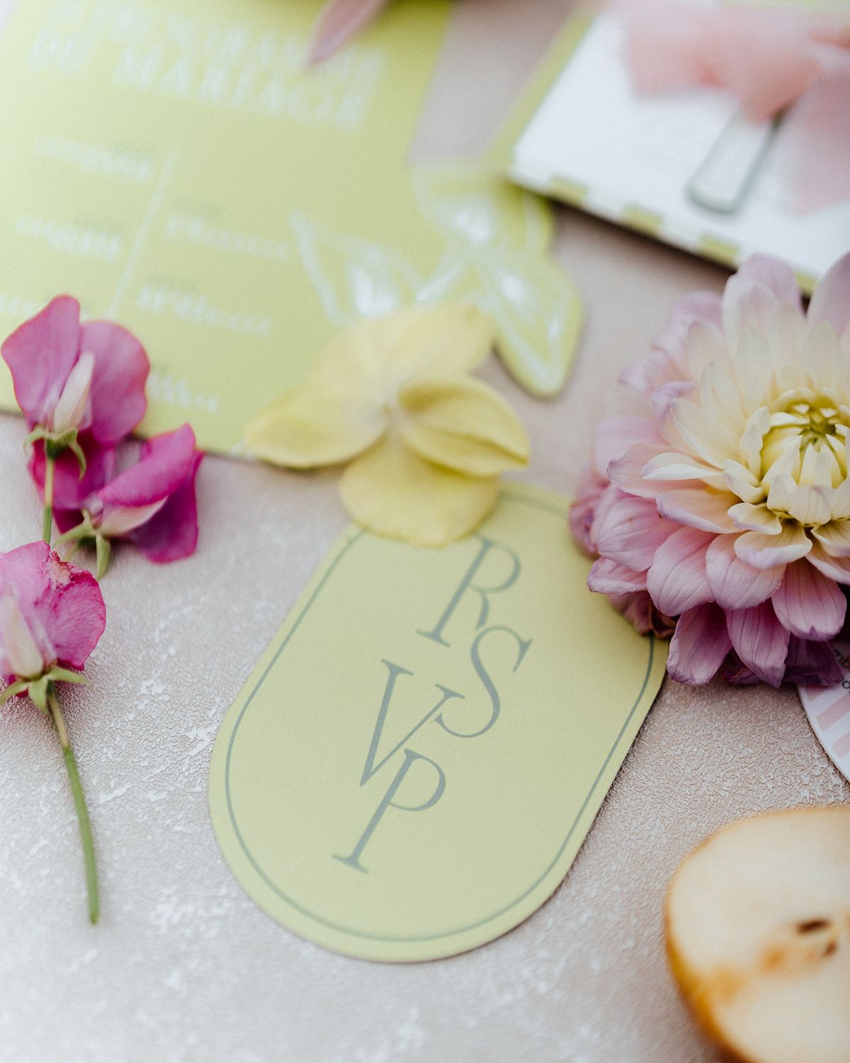 Soft yellow RSVP card lettered in white among sweet peas, dahlias and a sliced pear