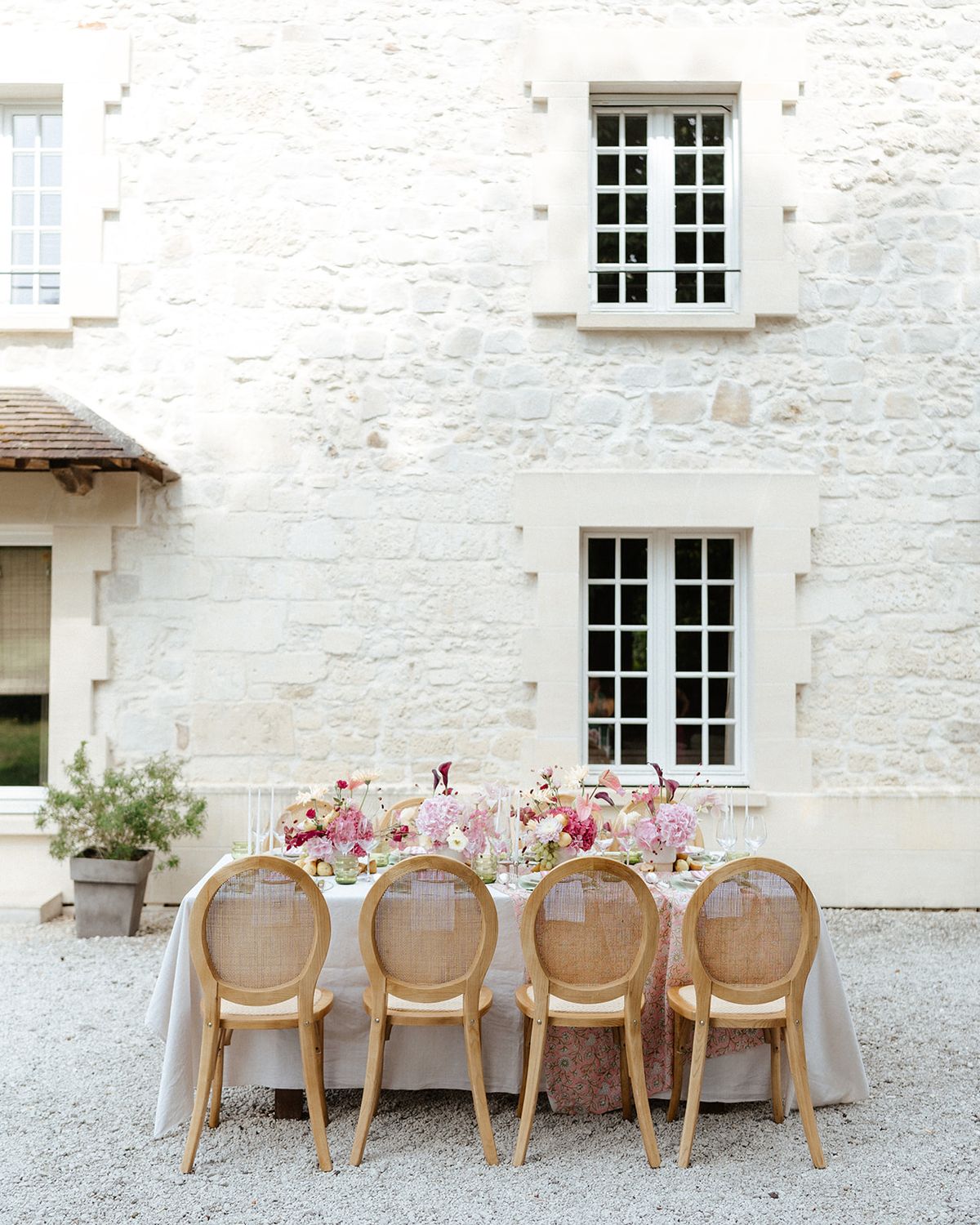 Long dinner table set with pale pink flowers against the white stone facade of La Porte d'Arcy