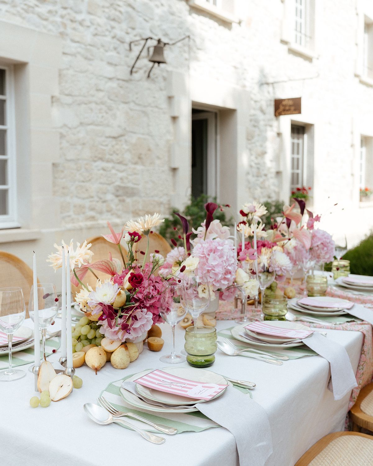 Dinner table along the stone wall with candles, pink flowers and fruit