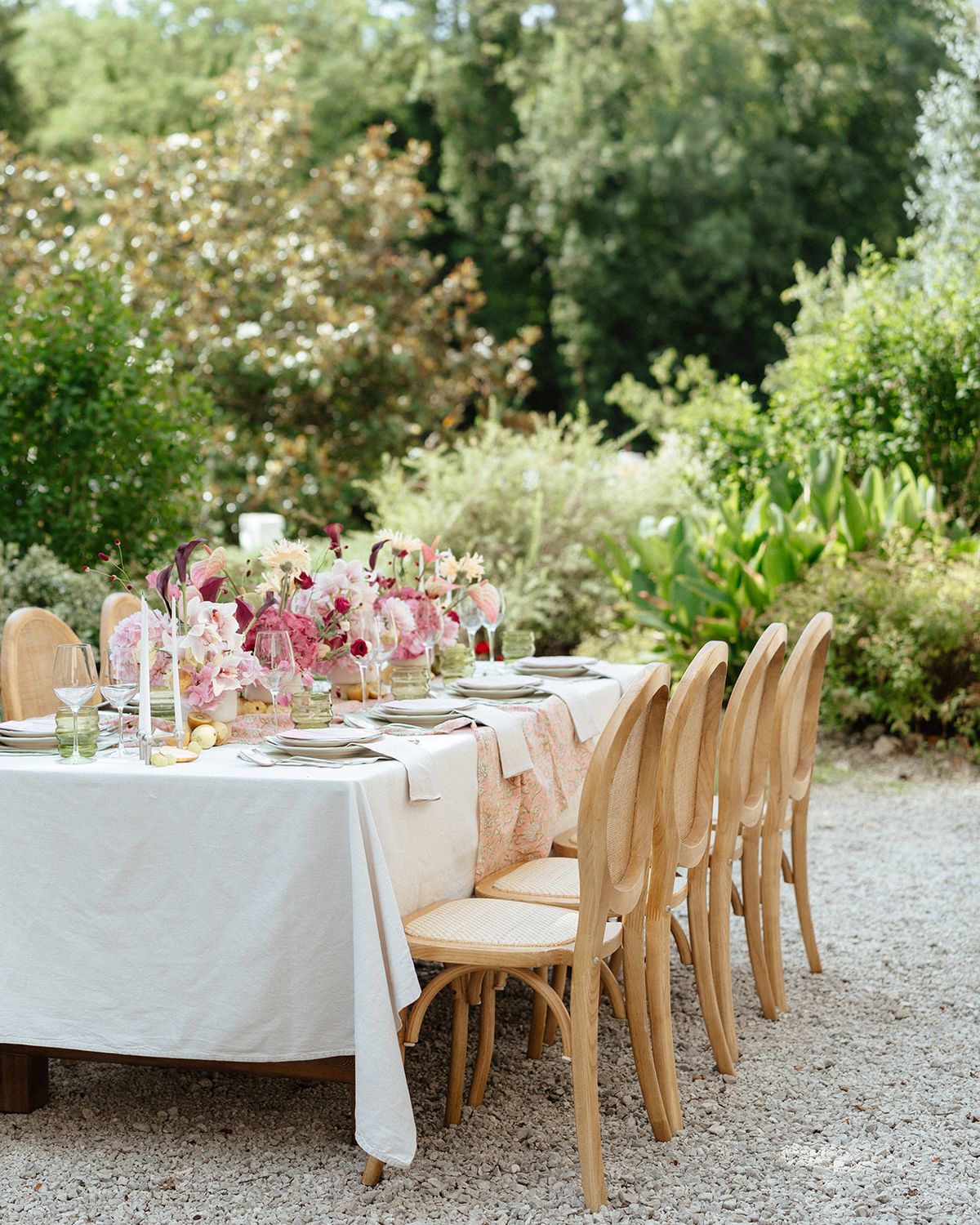 Long table laid with white linen, pink flowers and bentwood chairs in the garden
