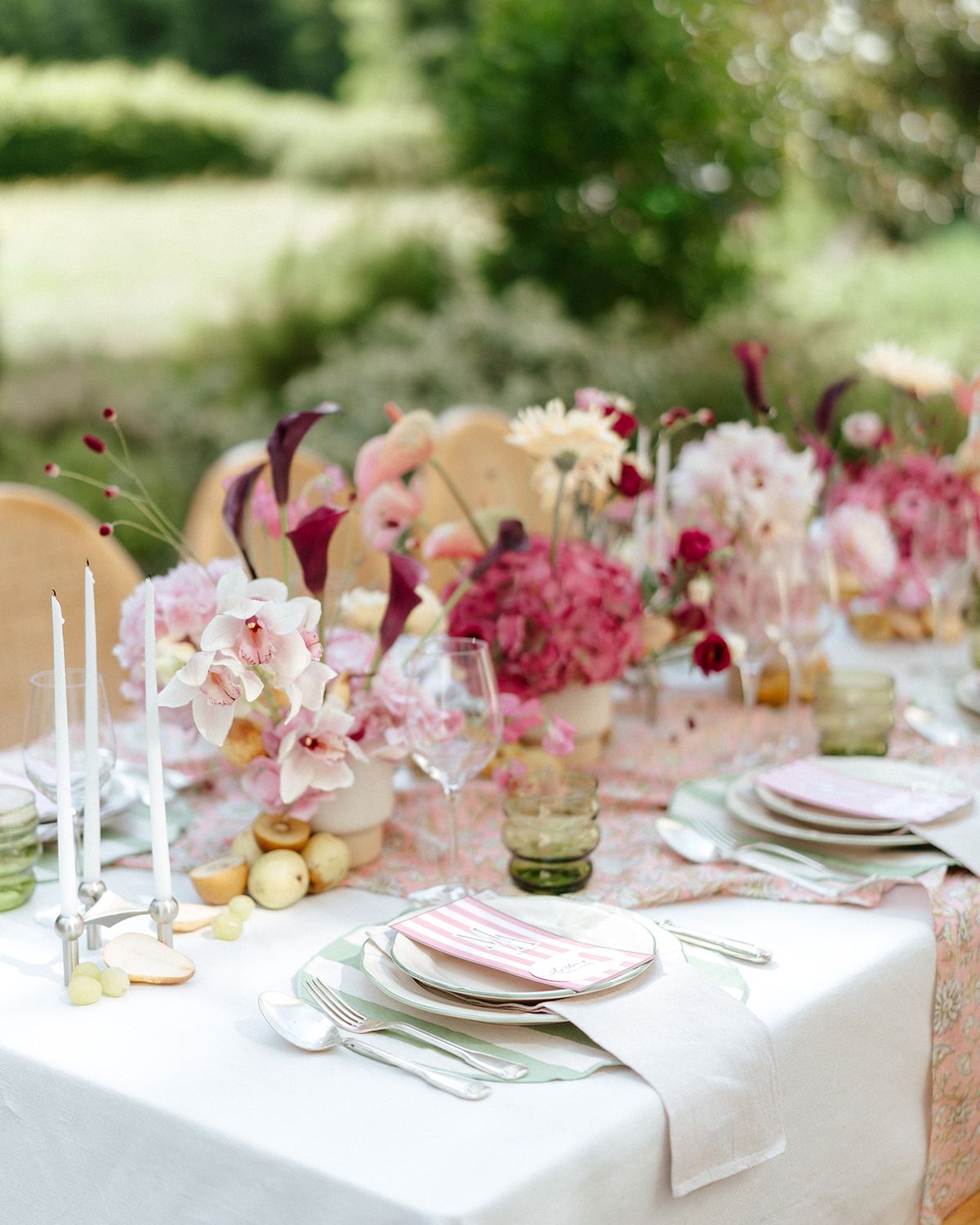 Dinner table with tapered candles, pink and burgundy flowers and scattered fruit