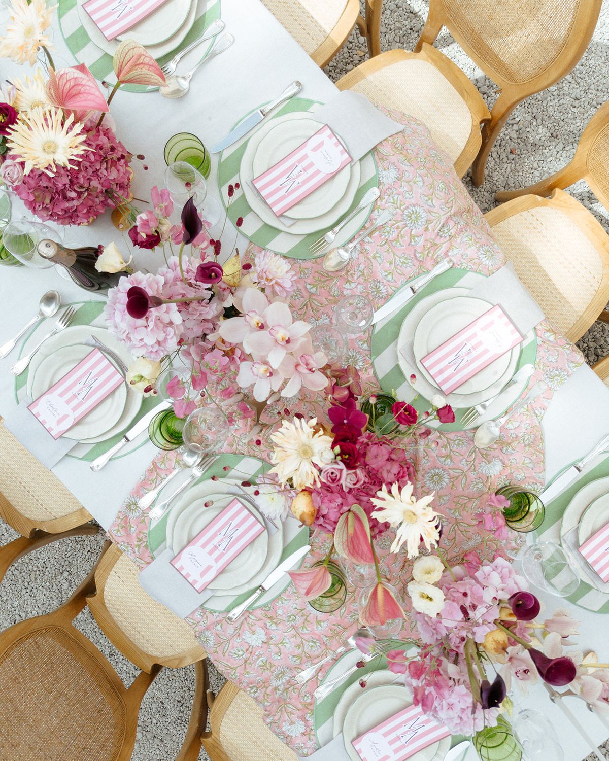 Overhead view of the table with a green striped runner, pink blooms and place cards