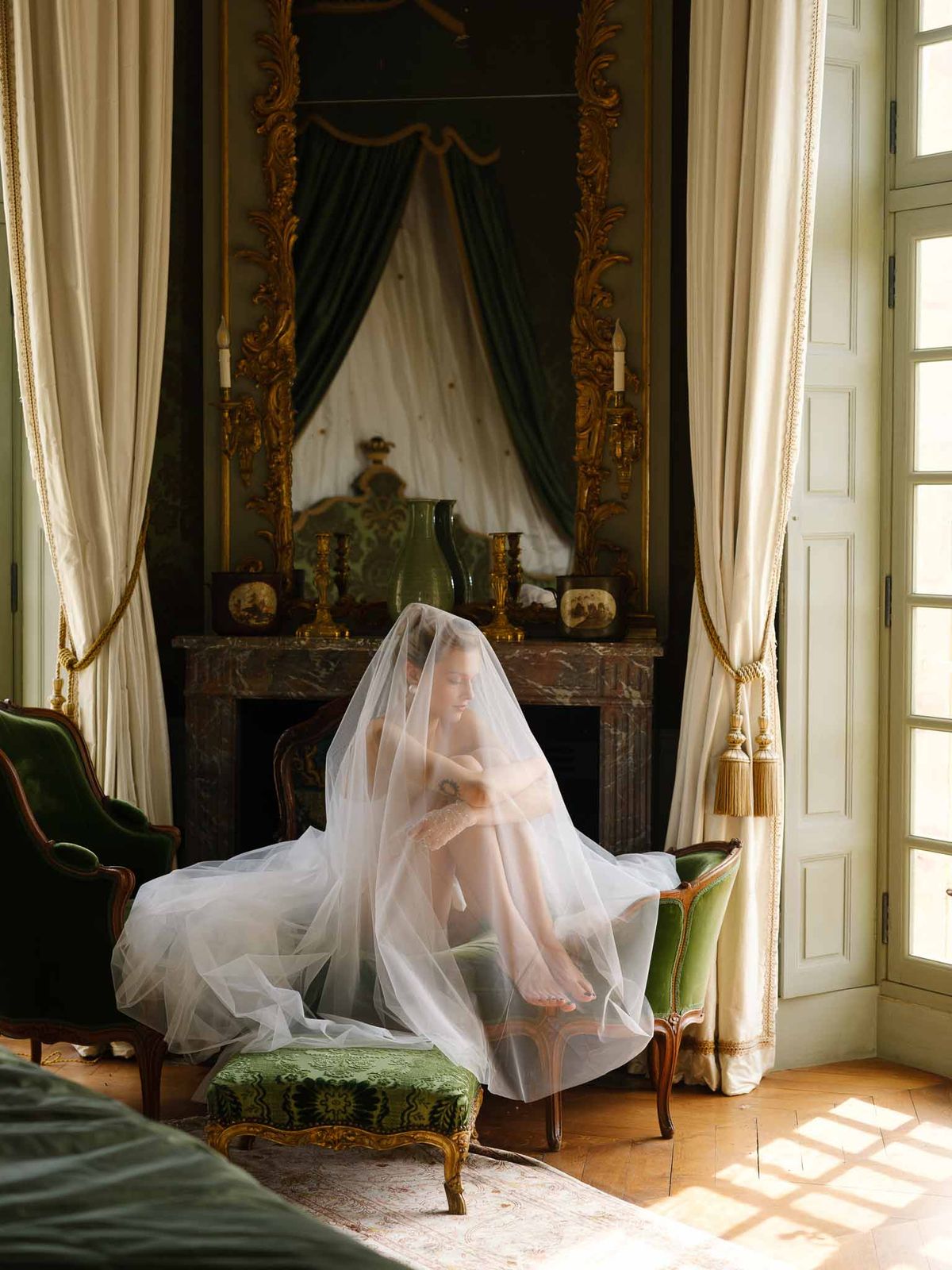 Bride seated with veil draped over her head in period room