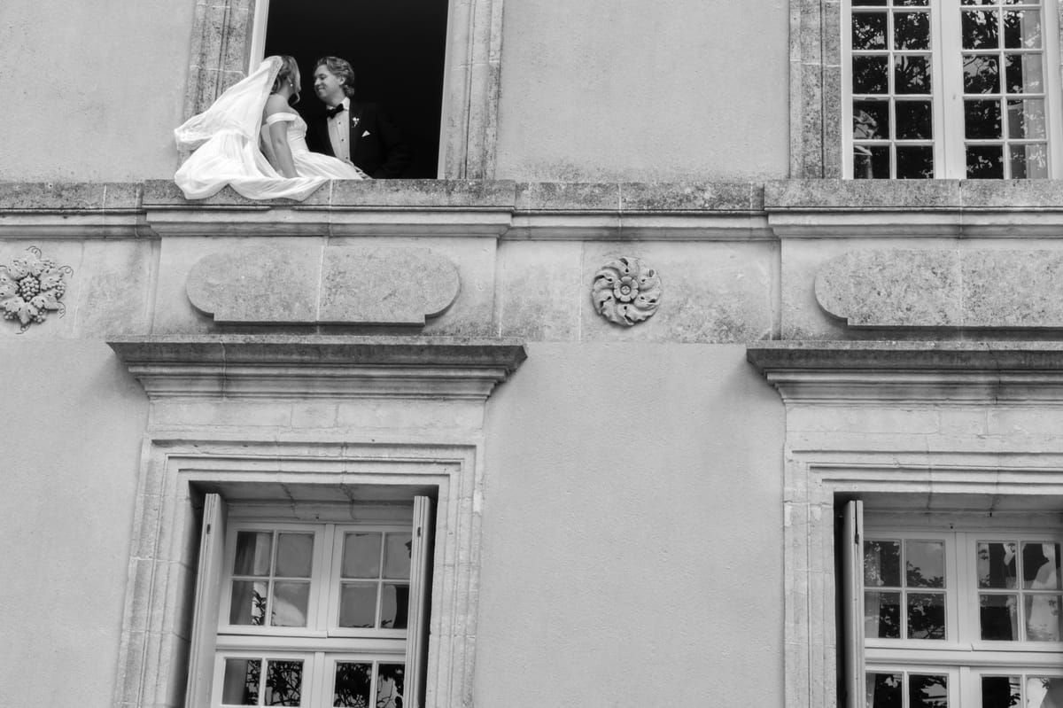 Seen from below, the couple kiss in an open upper window of a stone chateau as the veil drapes over the sill.