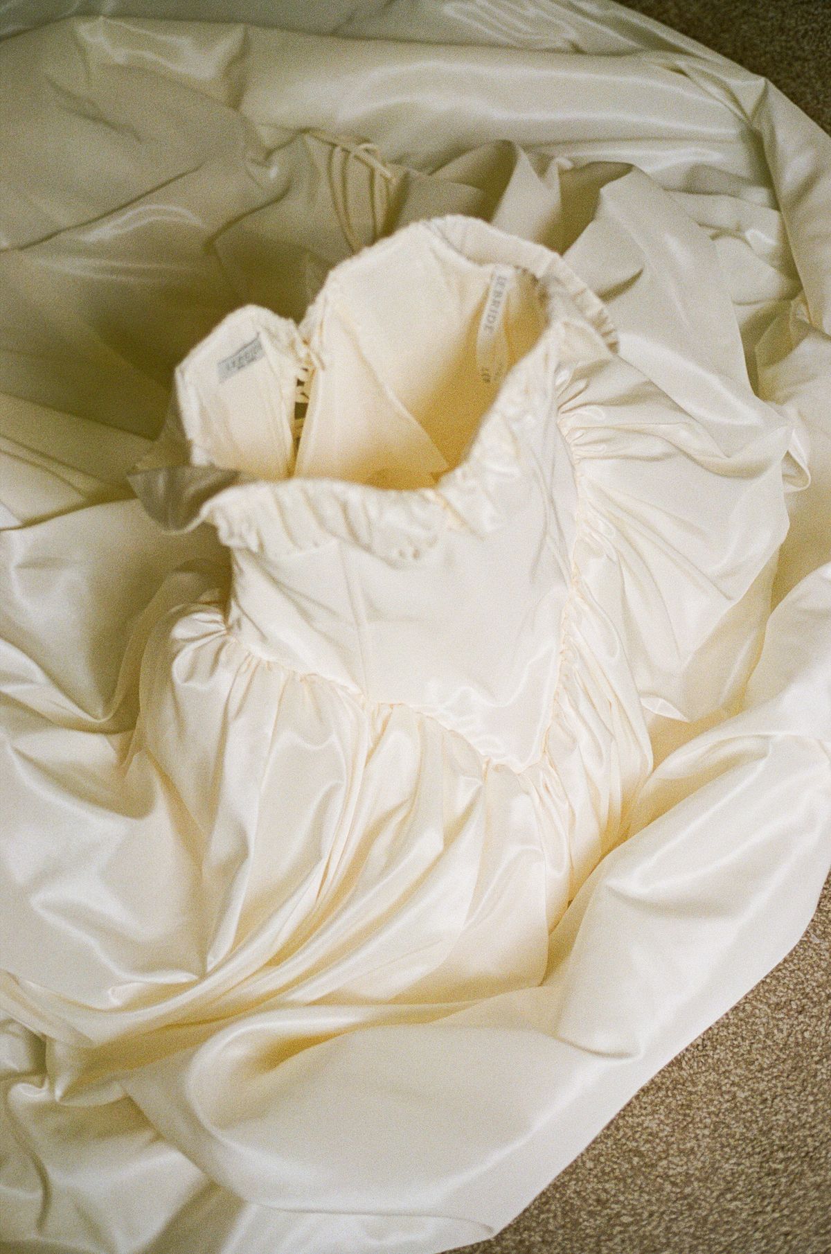 A cream satin wedding dress with a fitted bodice lies in soft folds, photographed from directly above.