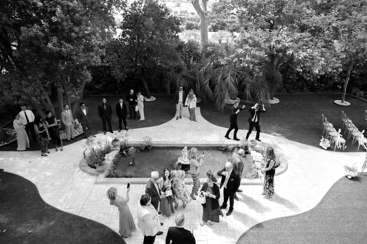 Seen from above, guests gather and talk on a curving paved terrace around a small pool, surrounded by trees.