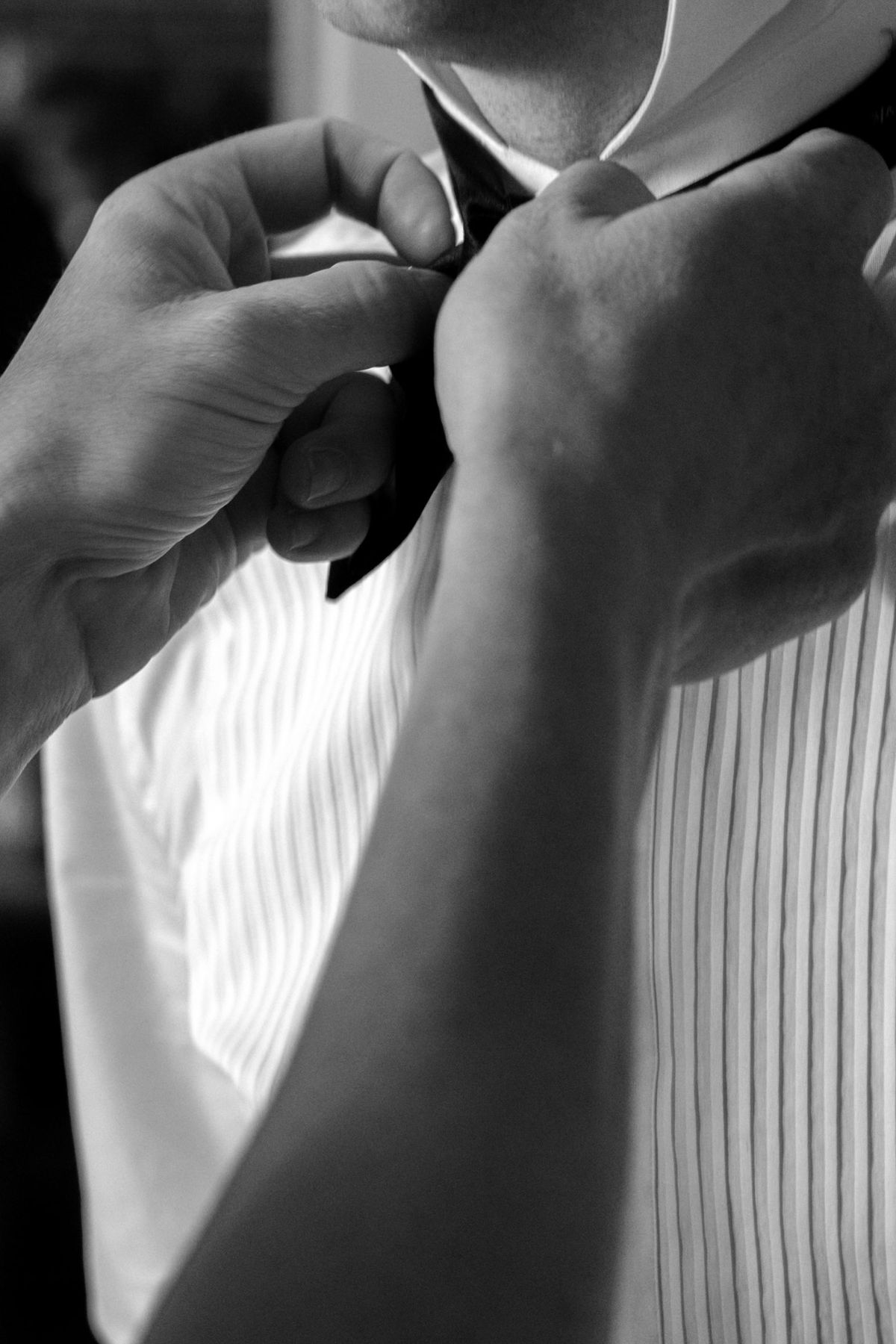 Close view of hands adjusting a bow tie at the collar of a white pleated dress shirt.