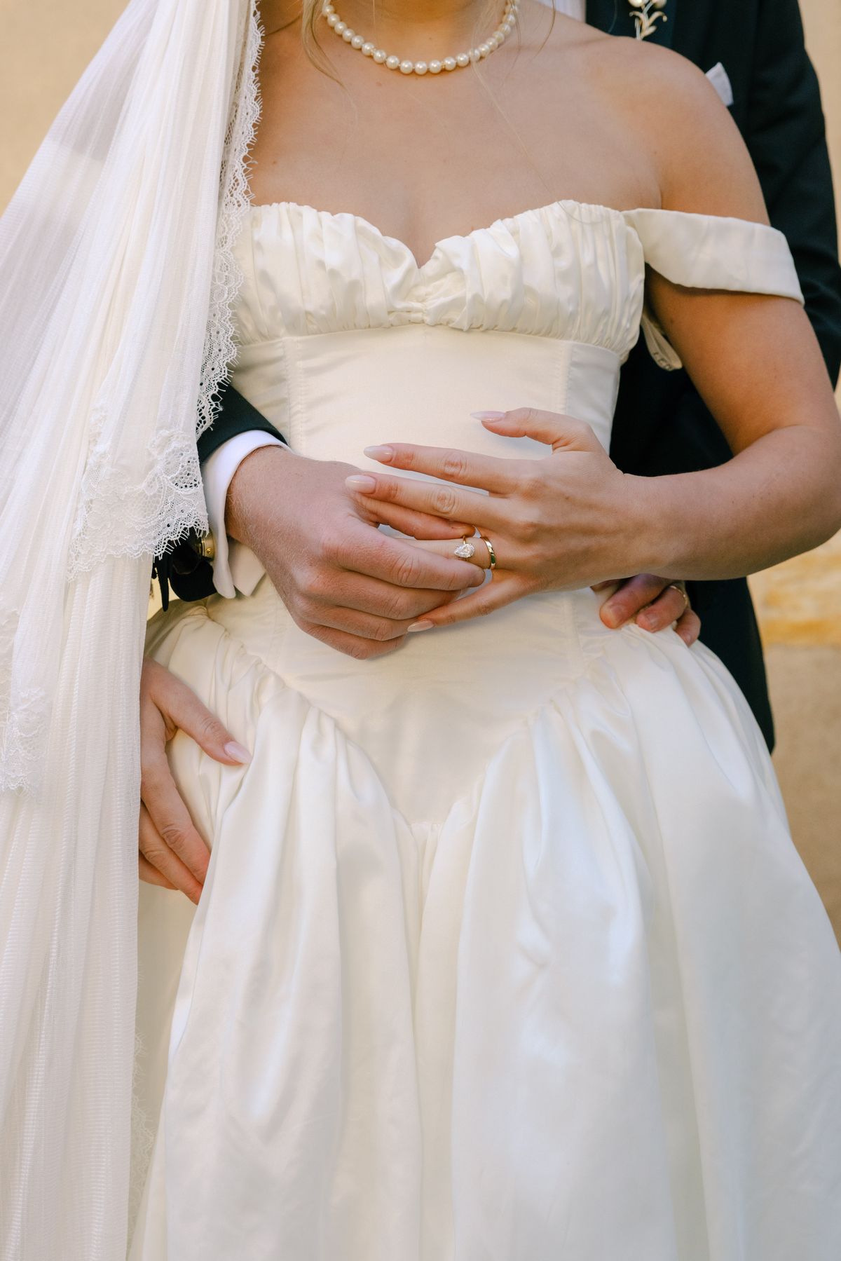 Close view of the bride in an ivory gown and veil, with the groom's arms around her waist and a ring on her finger.