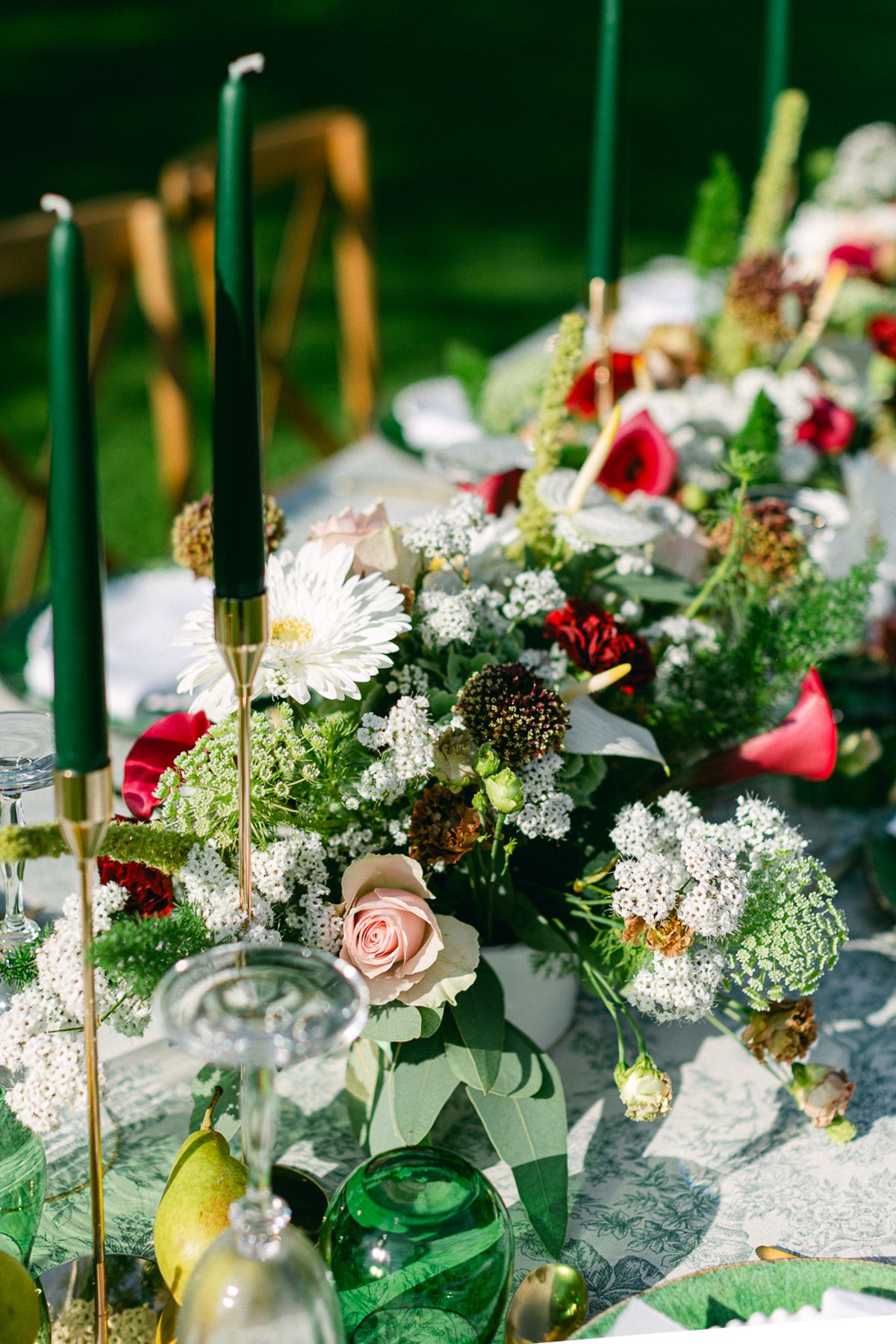 Close-up of a centrepiece of red, pink and white flowers with tall green candles and green glassware on a table.