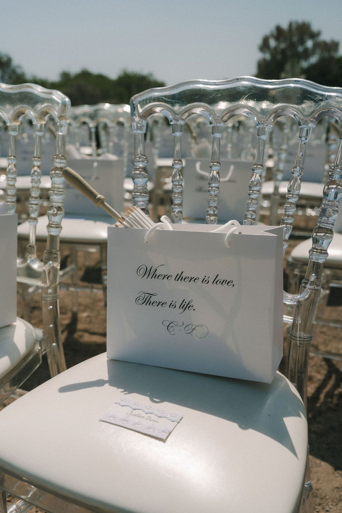 A white paper bag with printed script sits on the seat of a transparent chair, with more clear chairs behind.