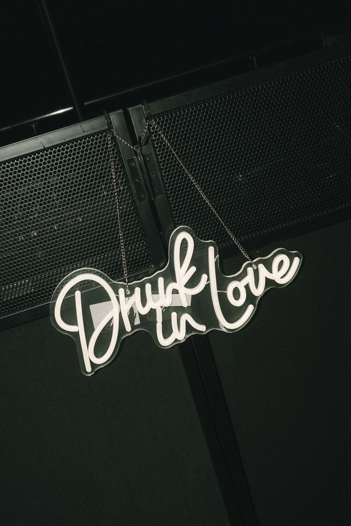 A white neon sign in cursive script reading Drunk in Love glows against a black speaker wall.