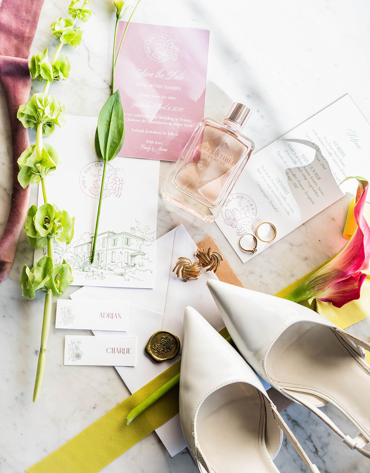 Flat lay of stationery, rings, bridal shoes and green blooms on marble
