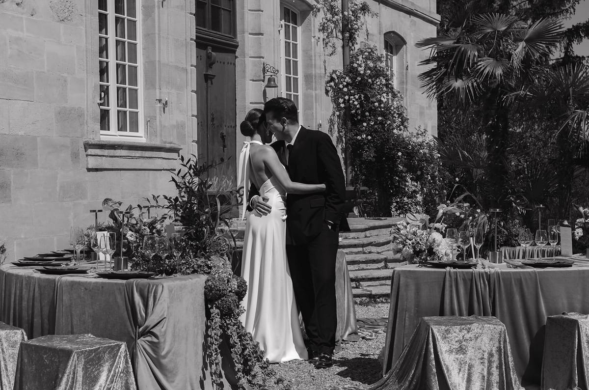 Black and white portrait of a couple embracing beside the dressed tables at the chateau