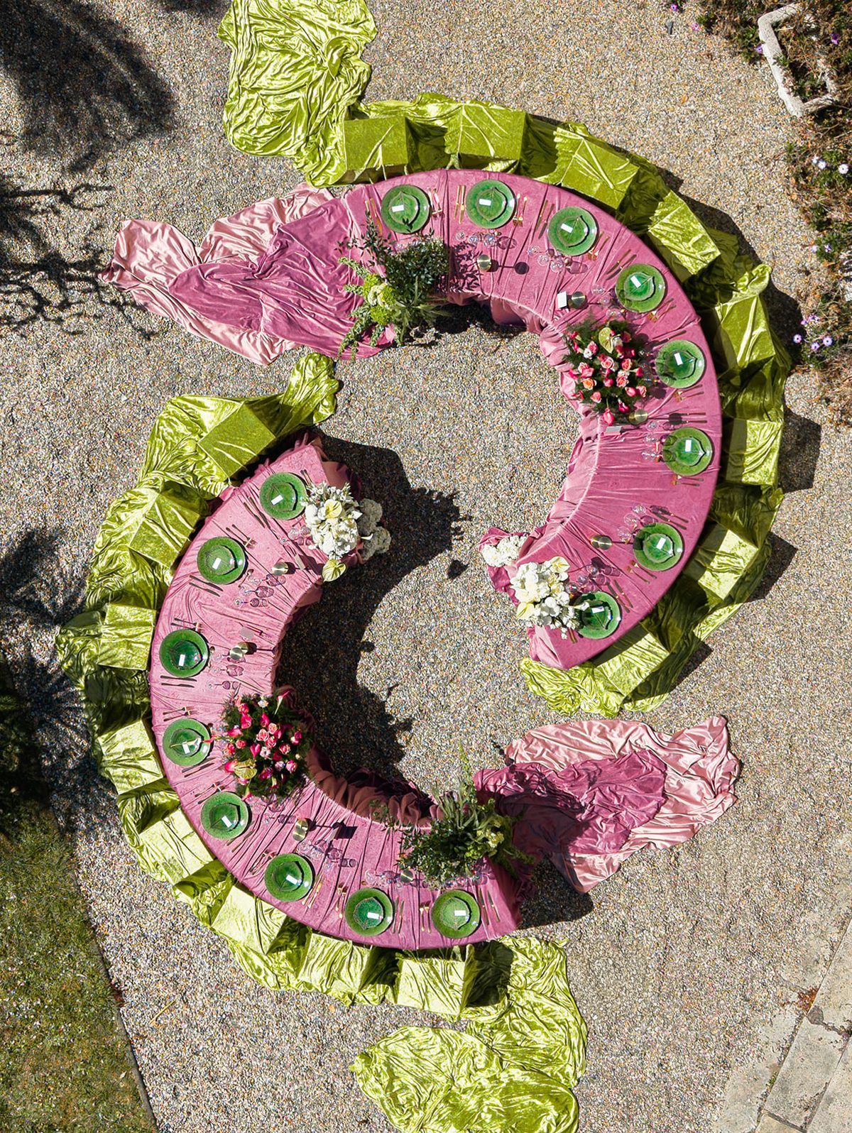 Overhead aerial of the two crescent tables in mauve and chartreuse velvet on the gravel courtyard