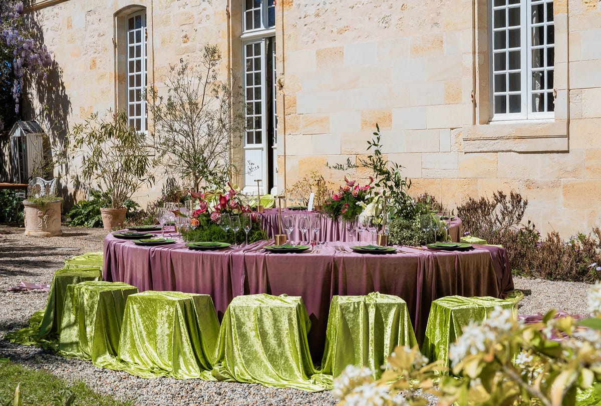 Two crescent reception tables in mauve velvet with chartreuse stools before the chateau's limestone facade