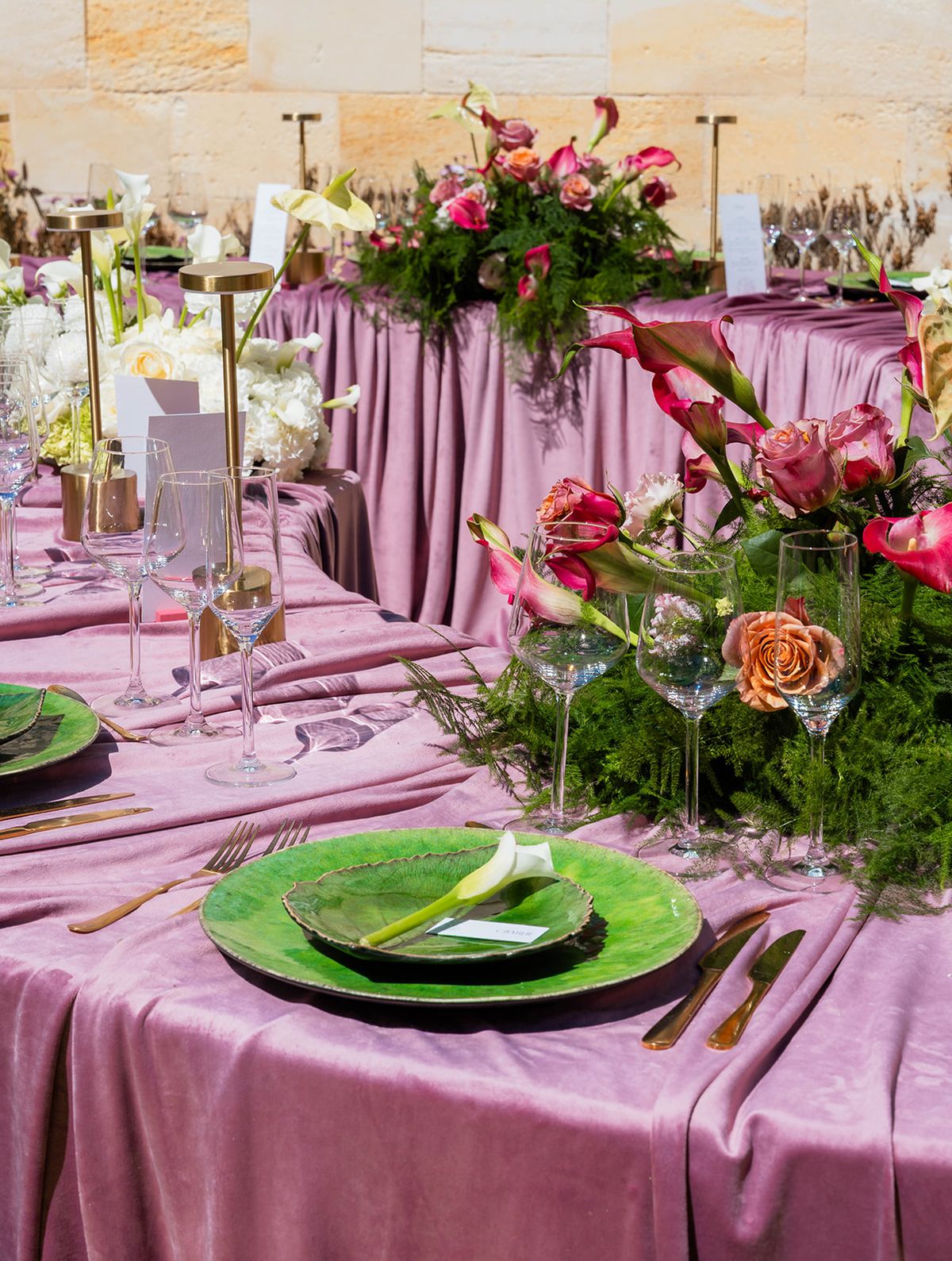 Table detail with green glass plates, gold flatware and layered floral arrangements along the crescent table