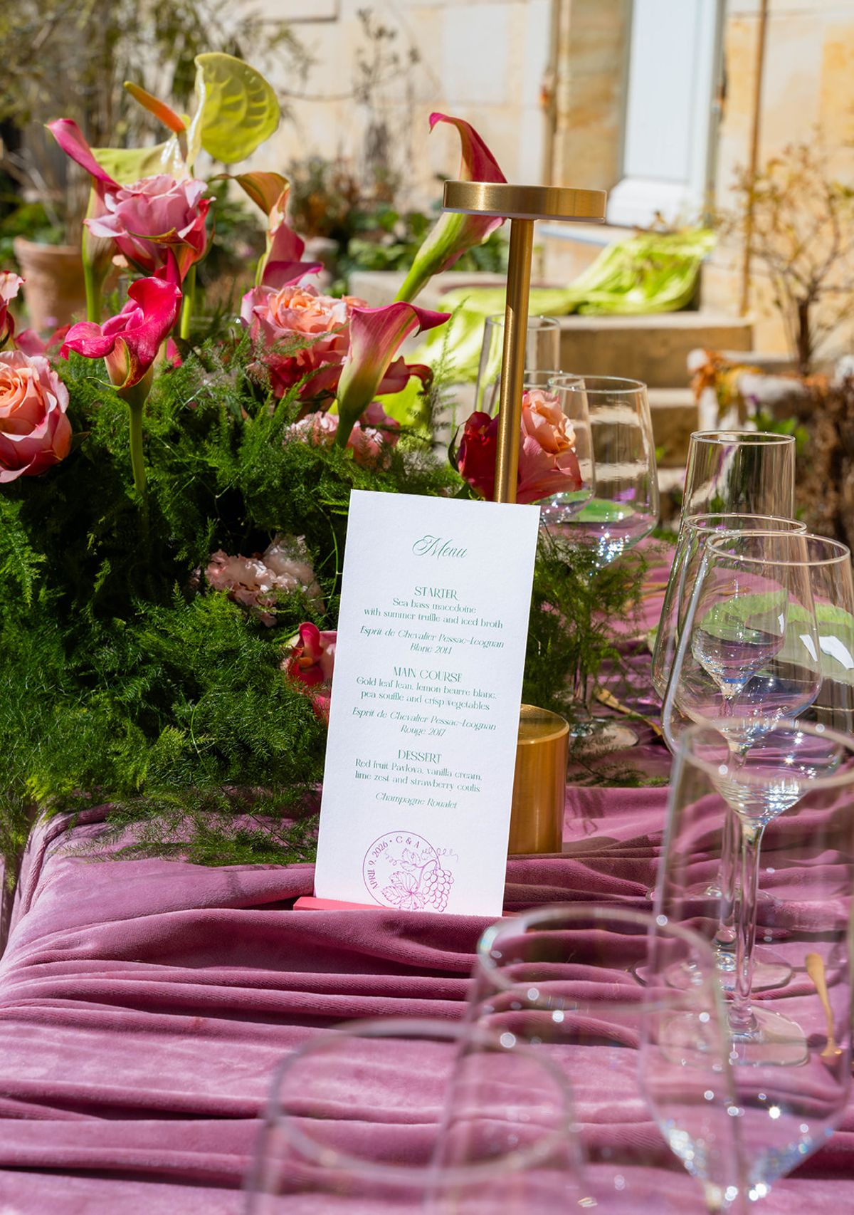 Menu card, glassware and floral arrangements along the mauve velvet table in spring sunlight