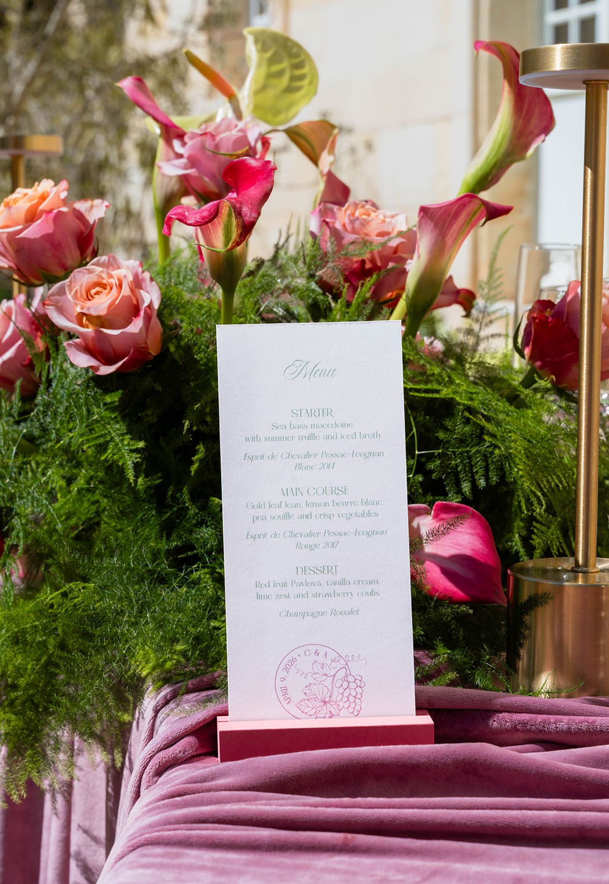 A printed menu card standing among ferns and coral florals on mauve velvet