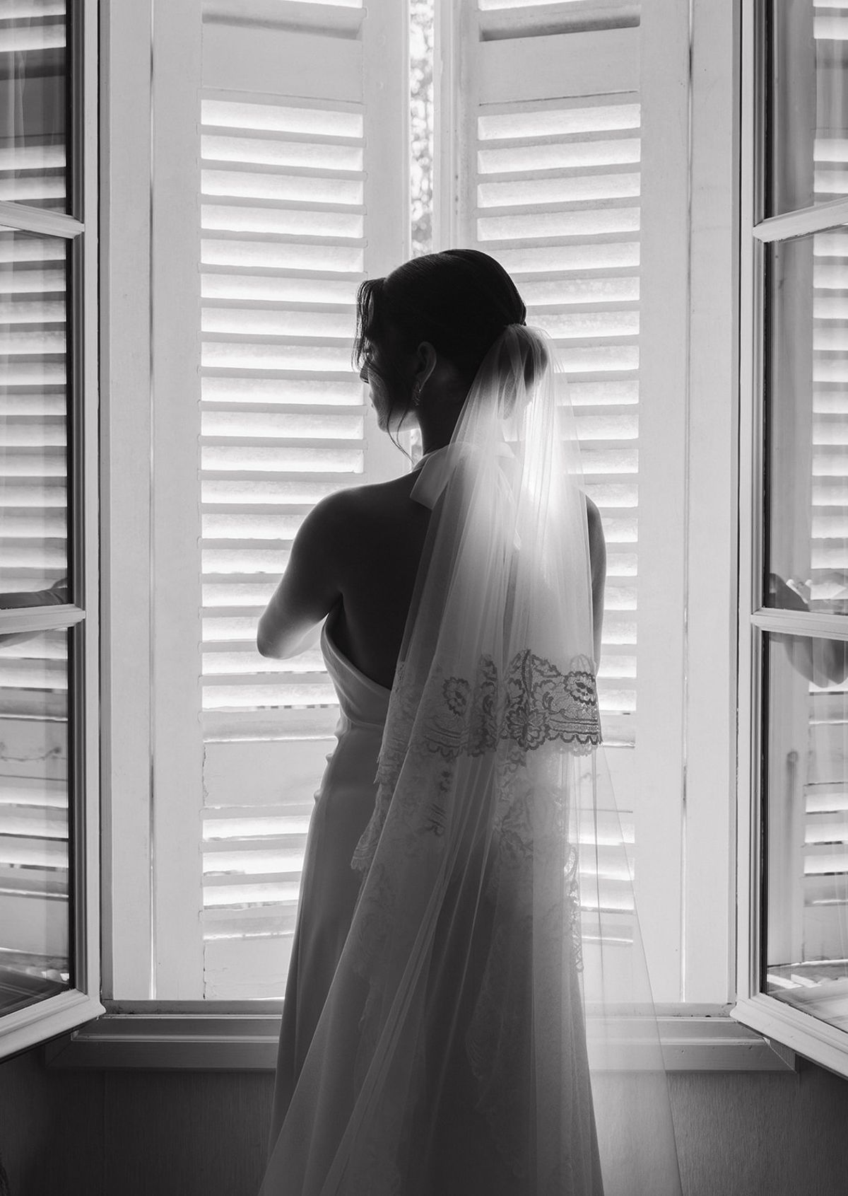 Black and white portrait of the bride in a lace-edged veil at a window