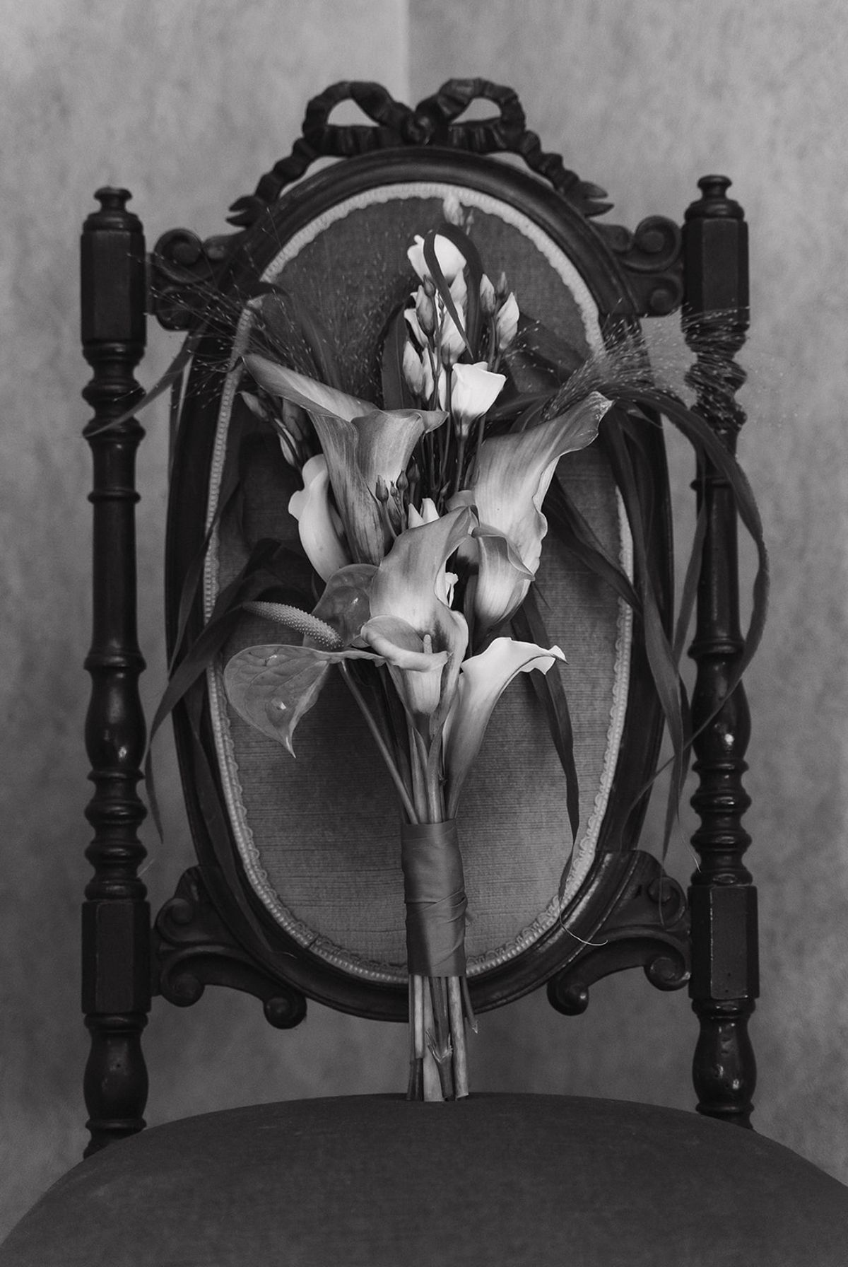 Black and white still life of a calla lily bouquet on an antique carved chair