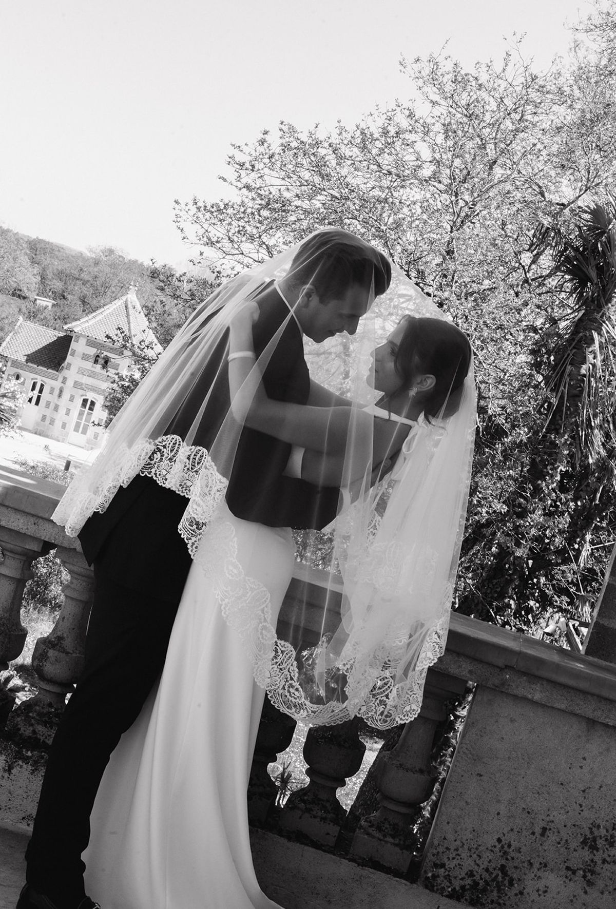 Black and white portrait of a couple beneath the veil on a stone balustrade