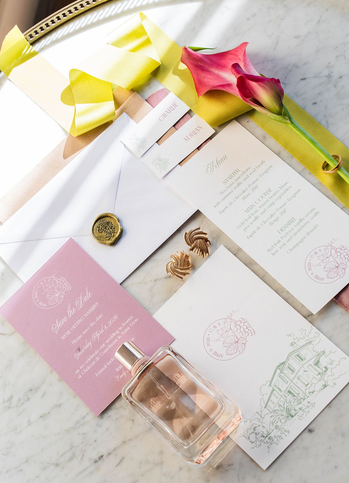 Flat lay of blush and chartreuse stationery with a wax seal, calla lily and perfume bottle on marble