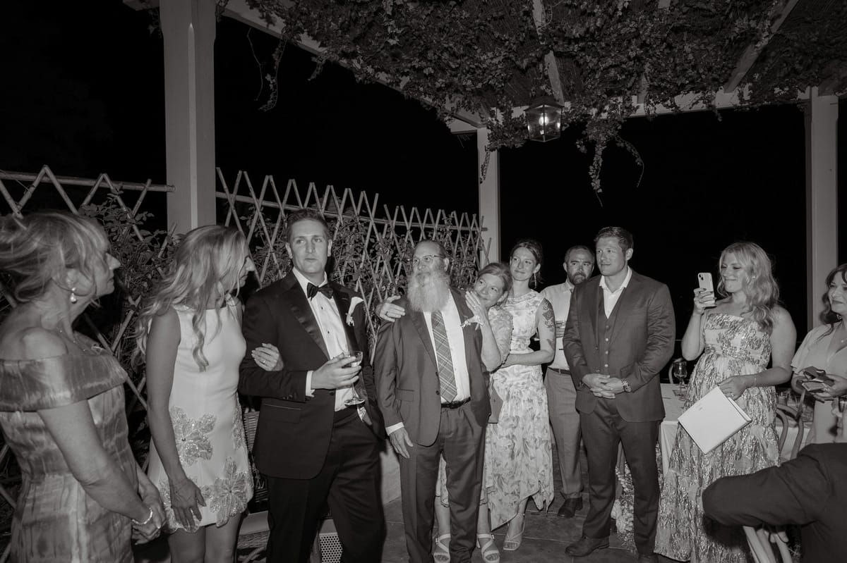 Black and white photo of Kirstin and Ryan with her father and guests under the pergola at night