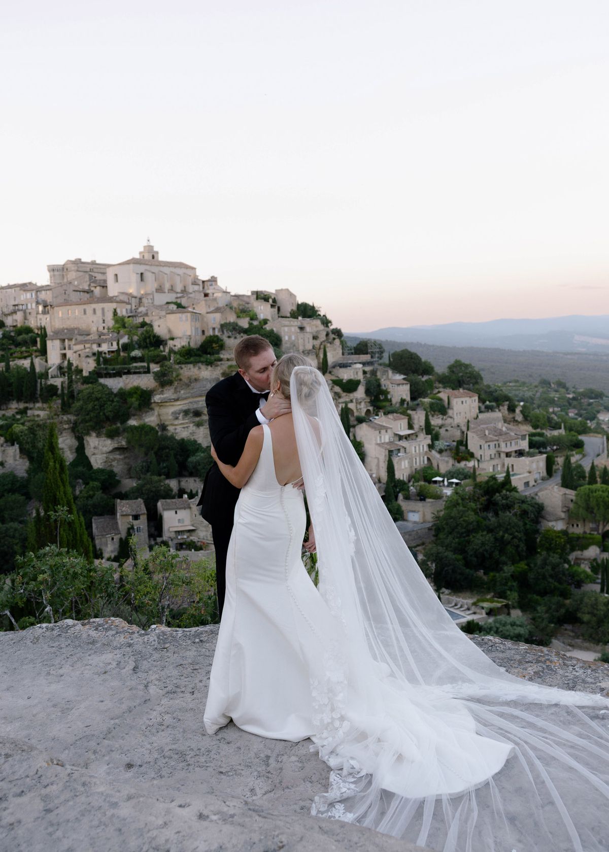 Kirstin and Ryan embracing on the ledge with the village behind