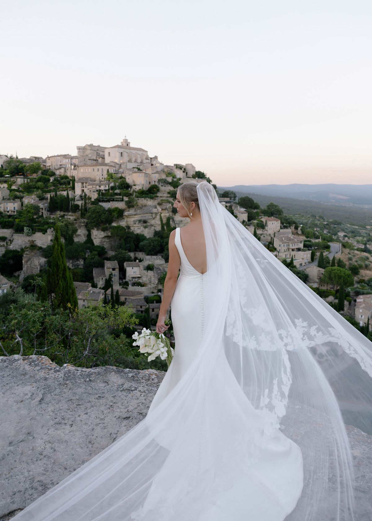 Bride from behind with her long veil above the village of Gordes