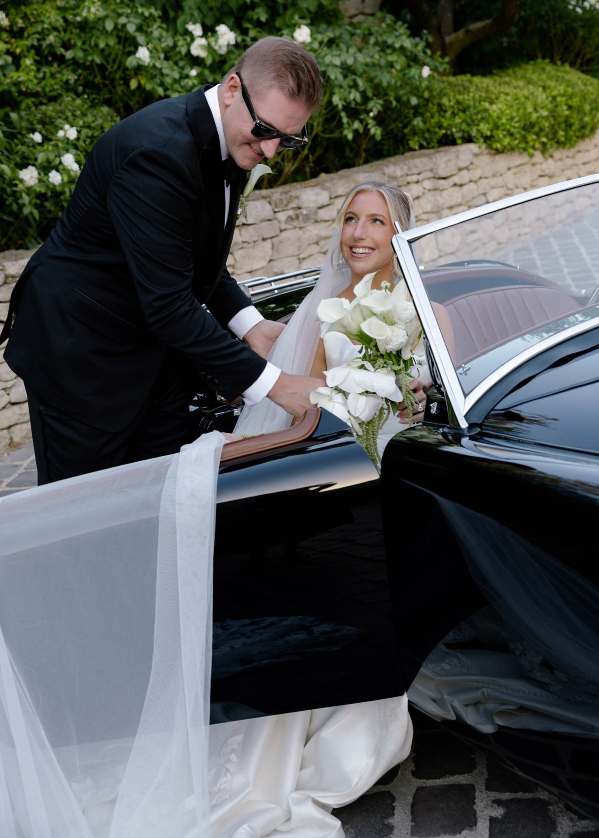 Groom helping the bride into a vintage convertible