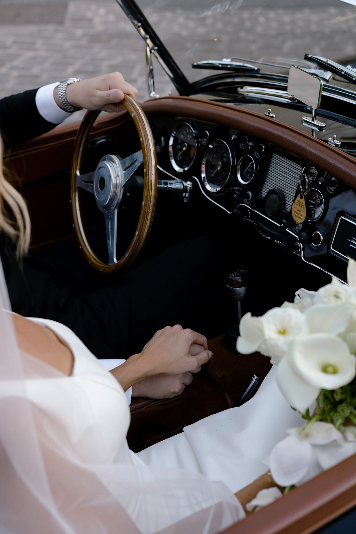 Groom's hand on the steering wheel beside the bride's bouquet