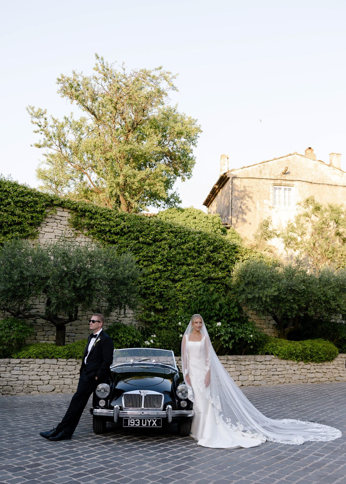Kirstin and Ryan with a black vintage convertible below a stone wall
