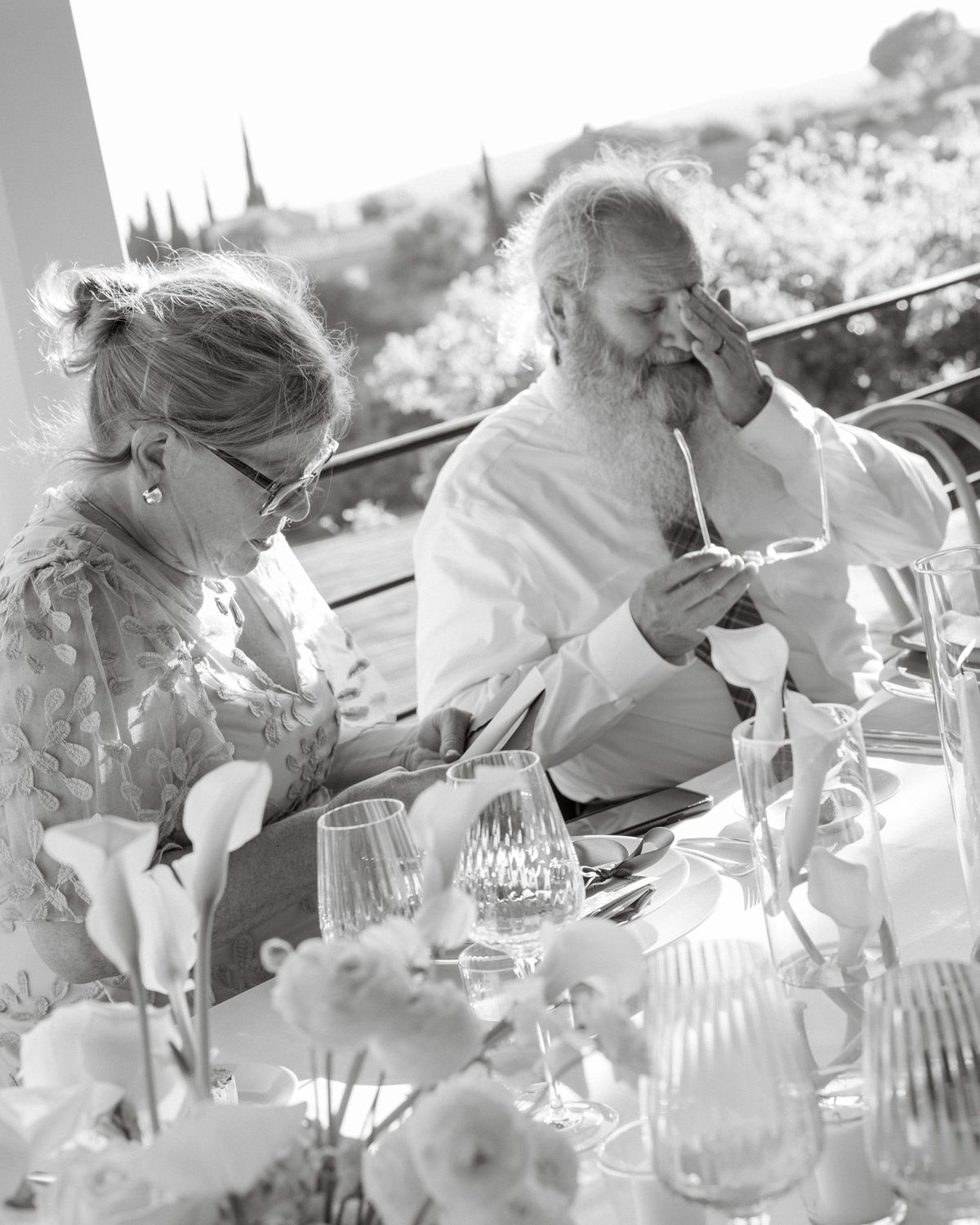 Black and white photo of the bride’s father wiping his eyes beside a guest at dinner