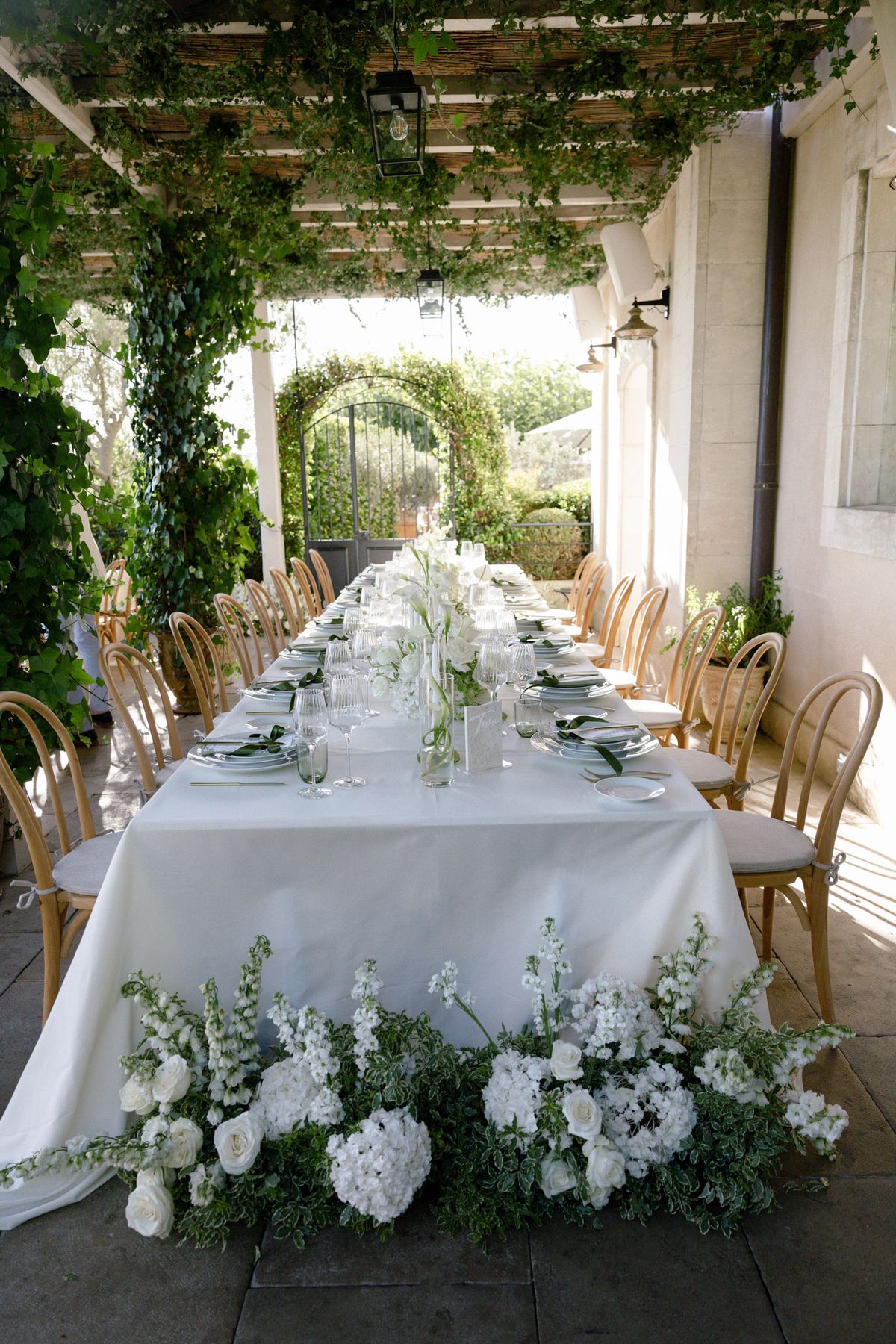 Long table under a pergola with white flowers at its foot